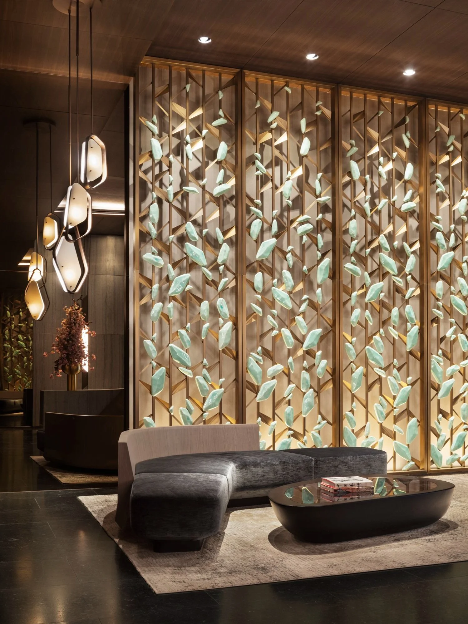 JGNA residential lobby detail of an illuminated jade-leaf brass screen with grey velvet seating and faceted pendants