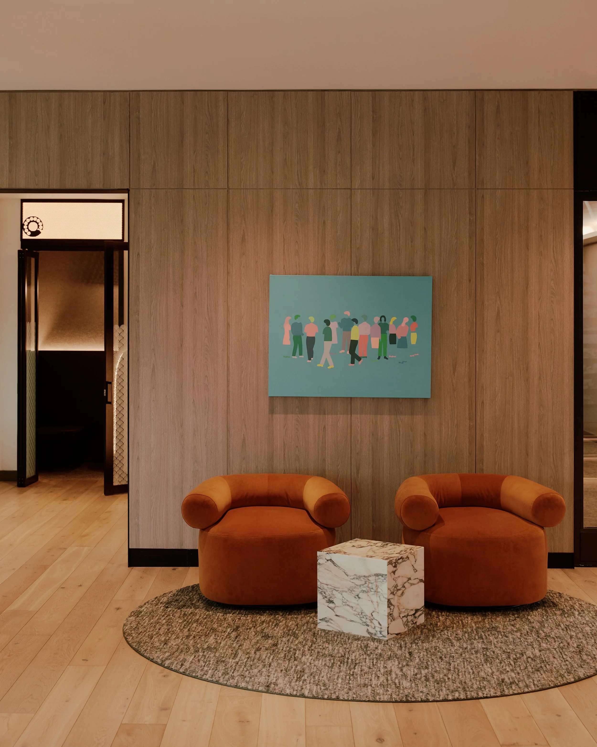 Lounge seating vignette with custom upholstered chairs, contemporary artwork, and wood-paneled walls at The Suffolk, a Lower East Side residential building, interiors by JG Neukomm Architecture