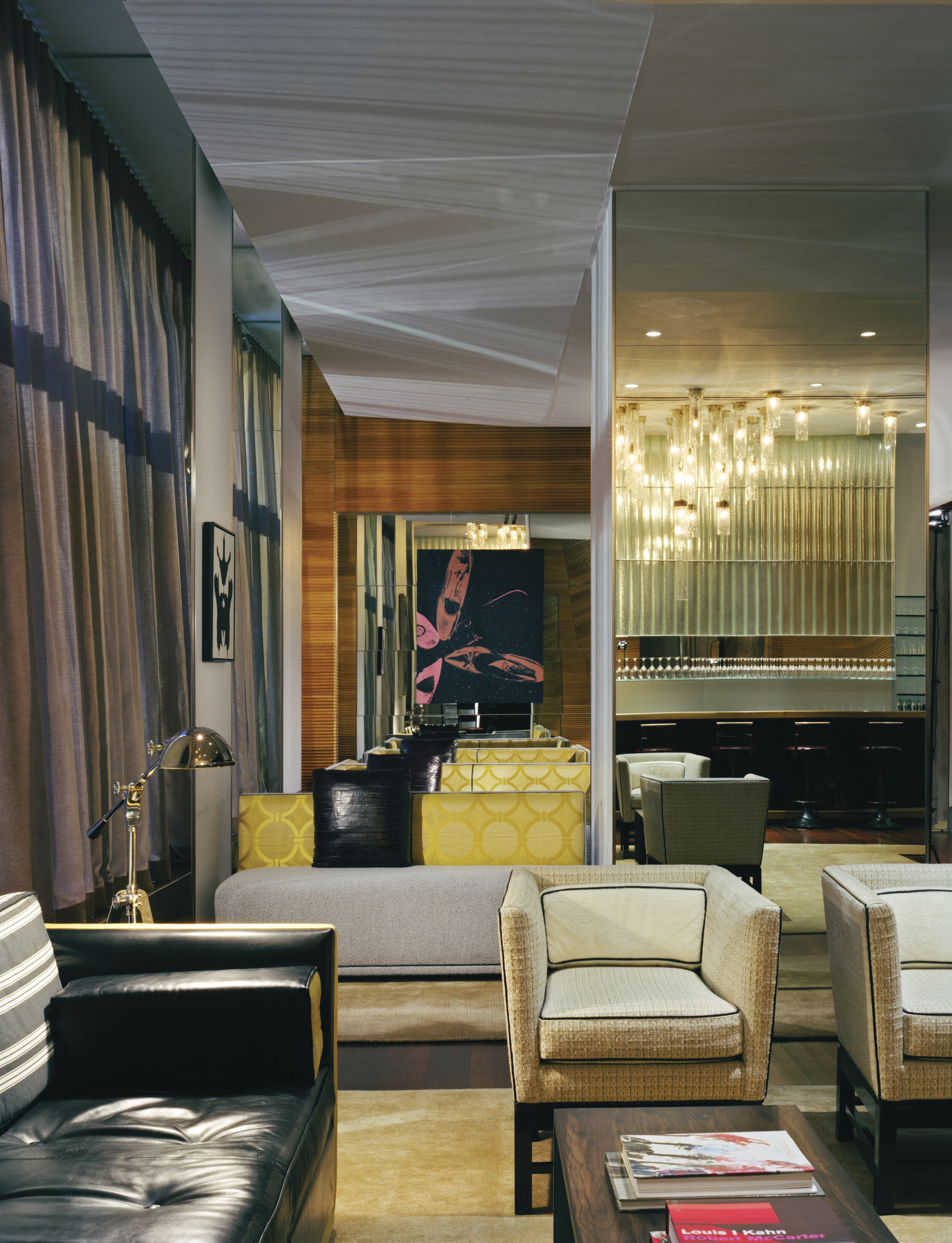 JGNA lounge with a black leather sofa, woven armchairs, walnut paneling, and a mirrored bar beyond