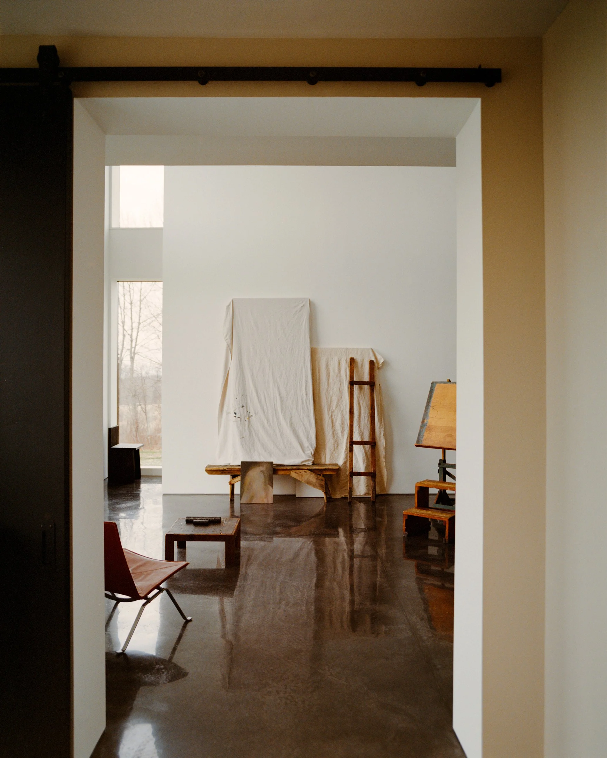 View through a sliding barn door into a light-filled room with polished concrete floors at a Ghent, NY home by JG Neukomm Architecture