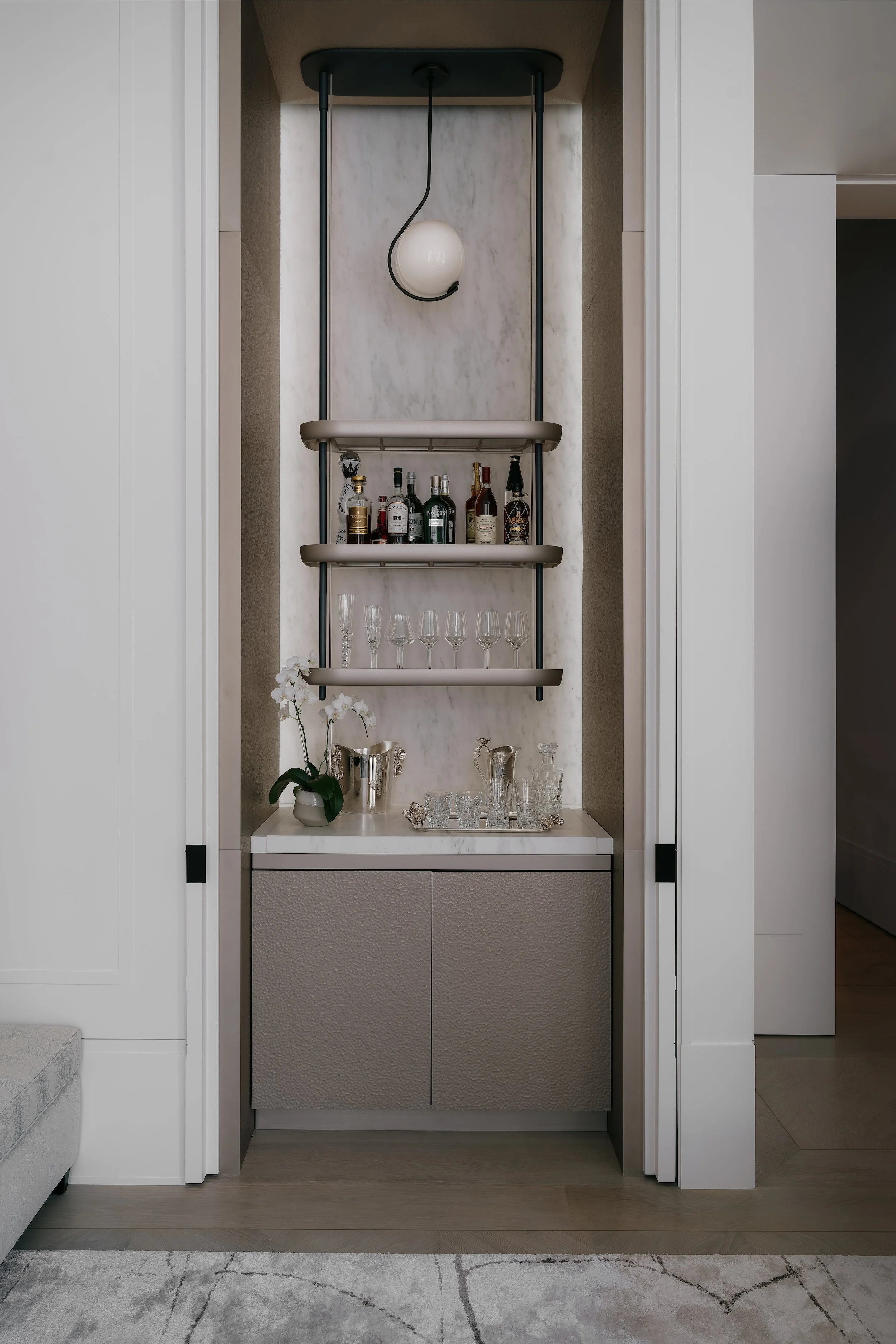 Built-in marble bar alcove with backlit shelving, glassware, and a spherical pendant light