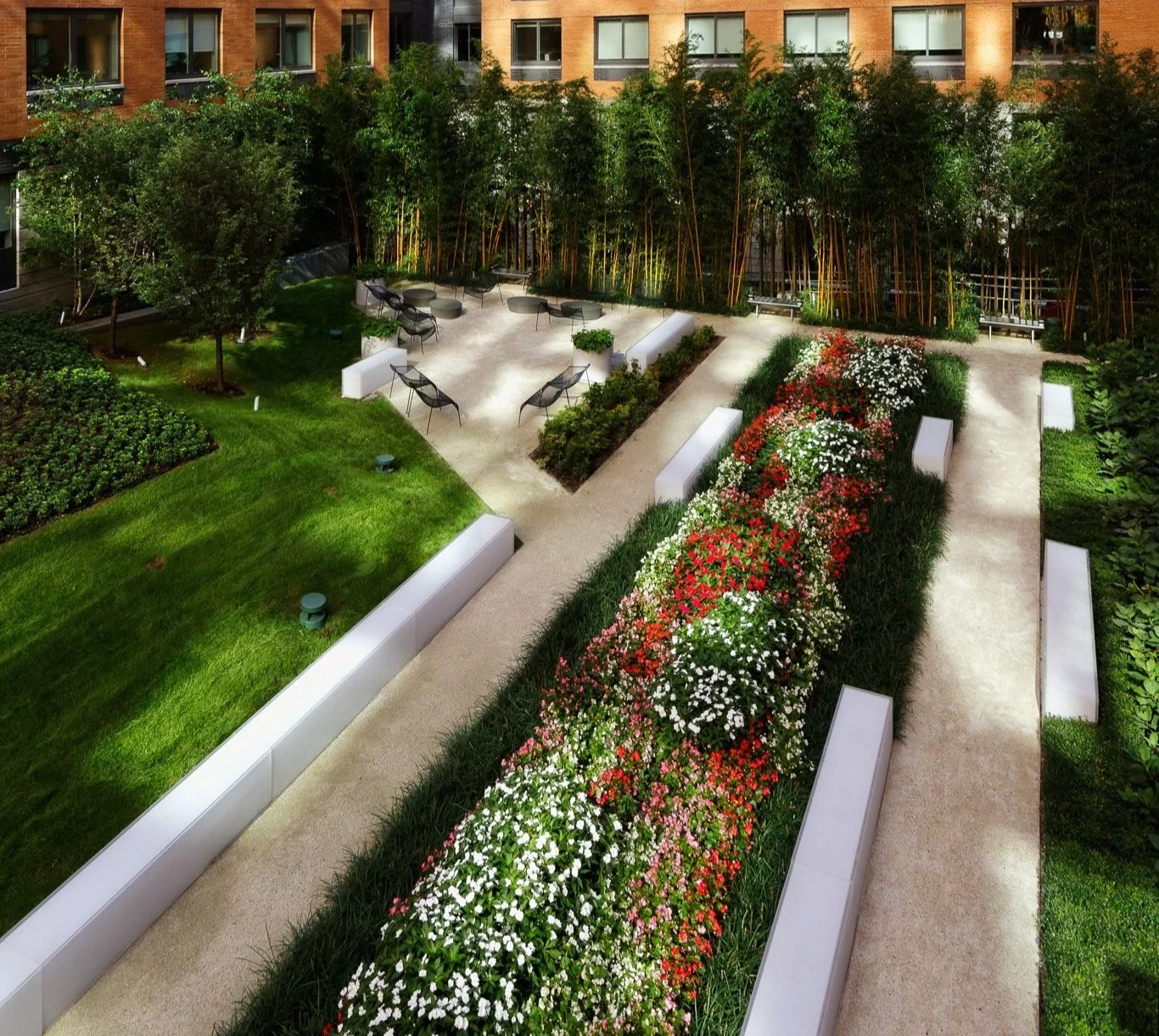 JGNA residential roof garden with terraced lawns, red and white flower beds, bamboo screening, and café seating