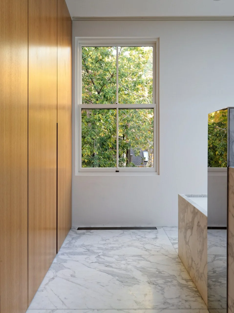 Minimalist master suite with floor-to-ceiling warm wood closet panels, marble floors, and garden window view in Fabien Baron Residence, West Village NYC by JG Neukomm Architecture