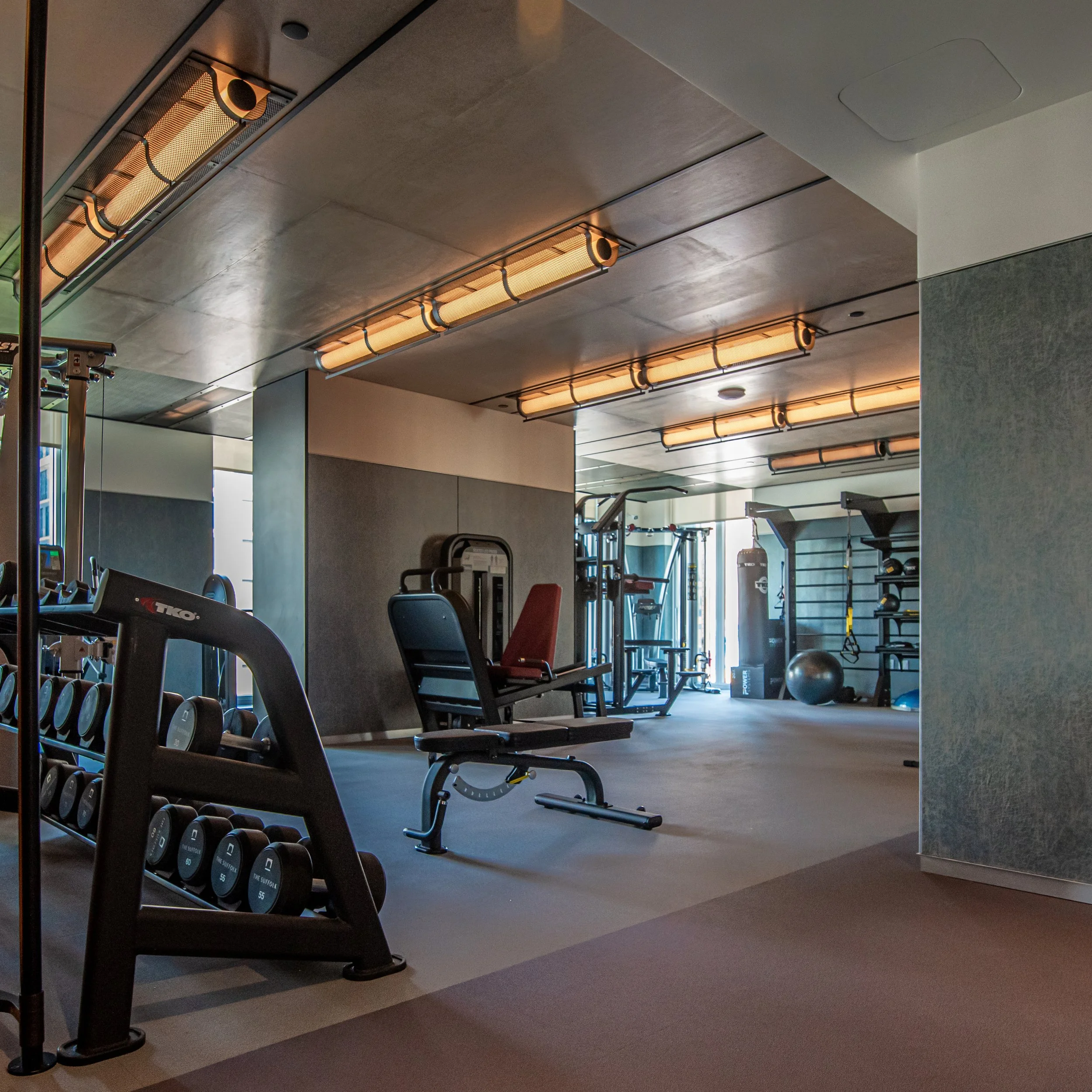 Fitness center with strength training equipment, functional workout areas, and integrated lighting at The Suffolk, a Lower East Side residential building, interiors by JG Neukomm Architecture