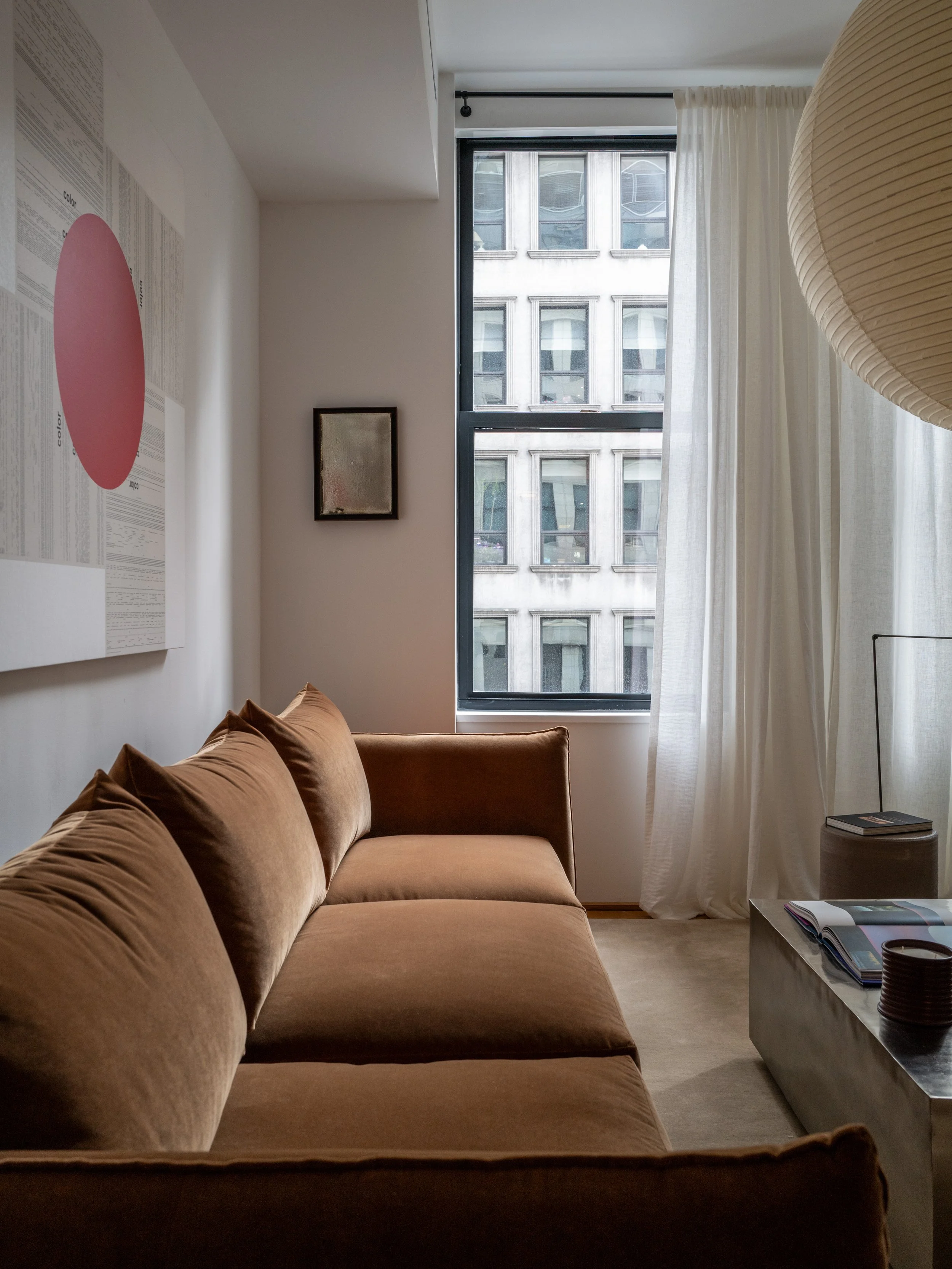 Velvet sofa in profile against a window bay with sheer curtains and city outlook