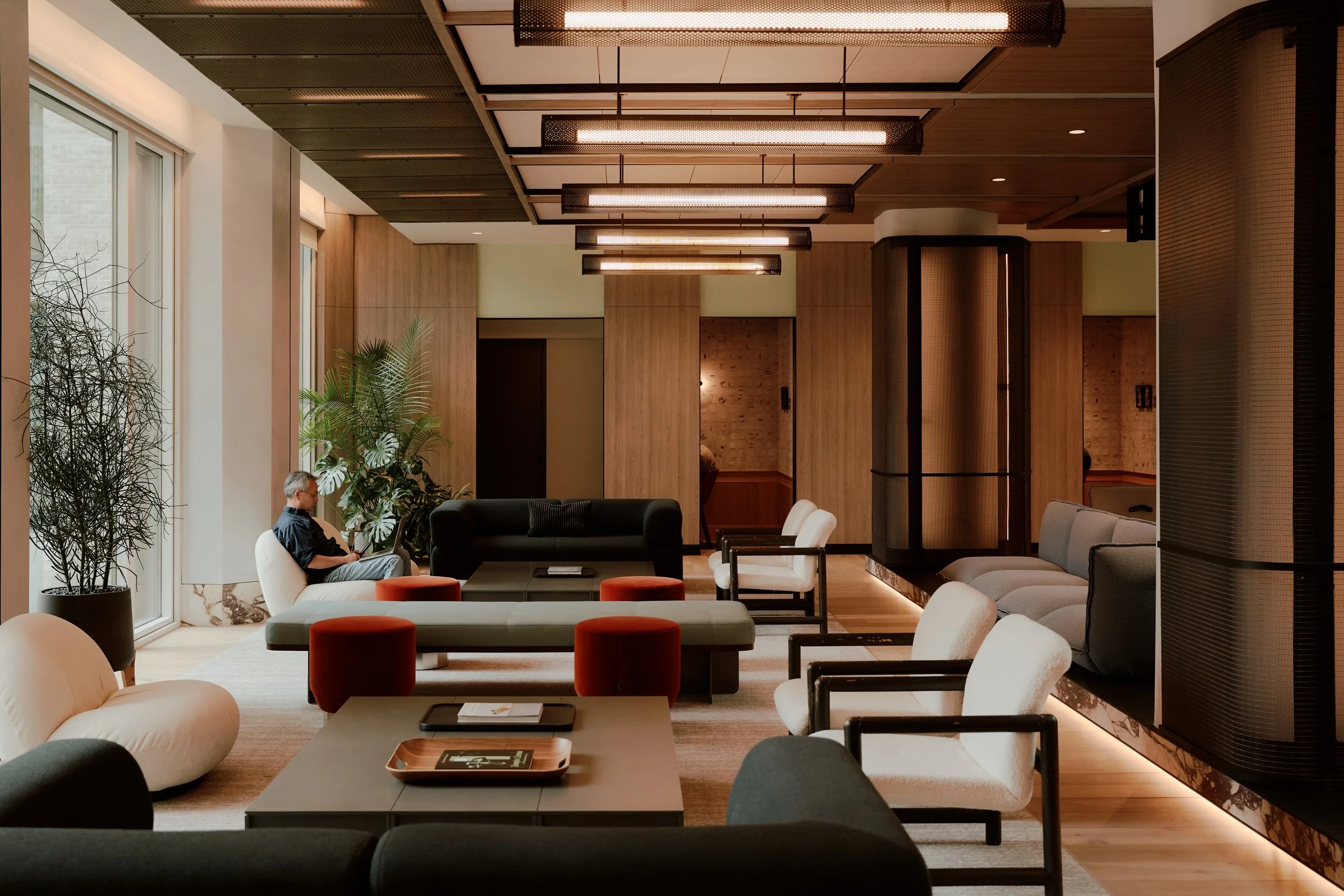 Residents lounge with custom seating, warm wood paneling, sculptural metal-clad columns, and linear pendant lighting at The Suffolk, a Lower East Side residential building, interiors by JG Neukomm Architecture