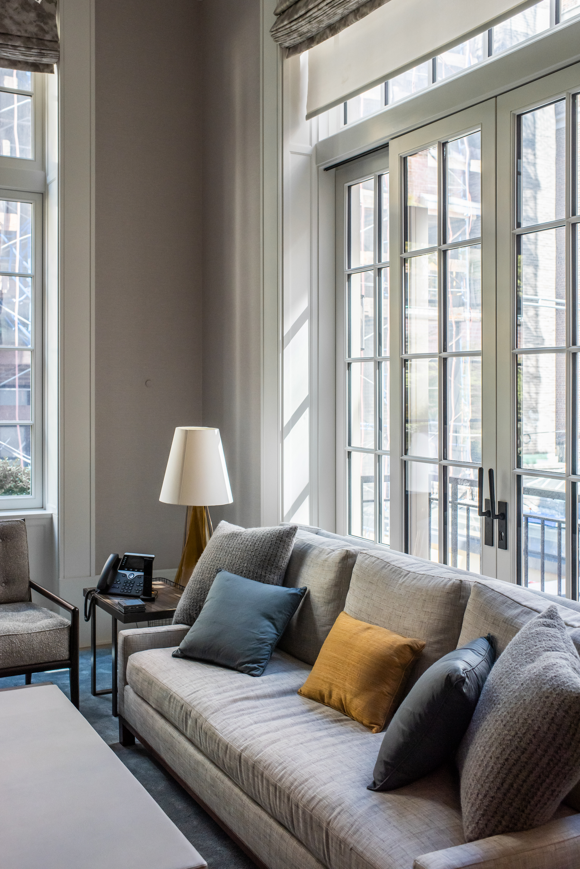Grey upholstered sofa with blue and ochre pillows beneath tall divided-light French windows