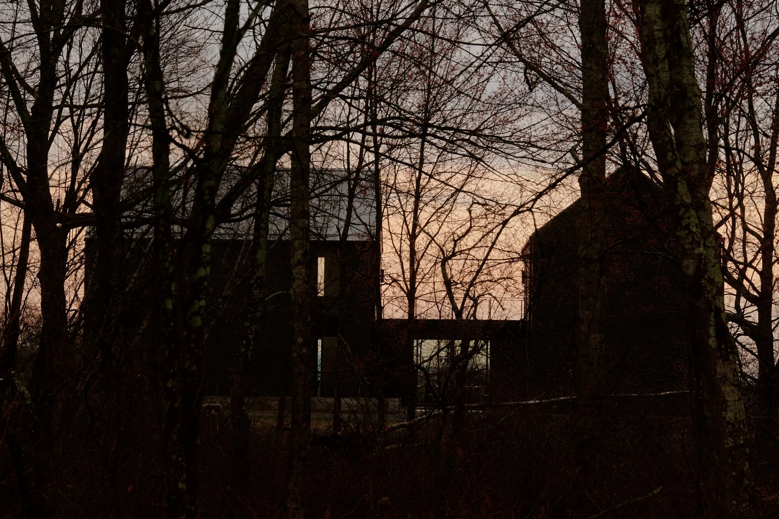 schoolhouse at dusk behind trees at a Ghent, NY home by JG Neukomm Architecture