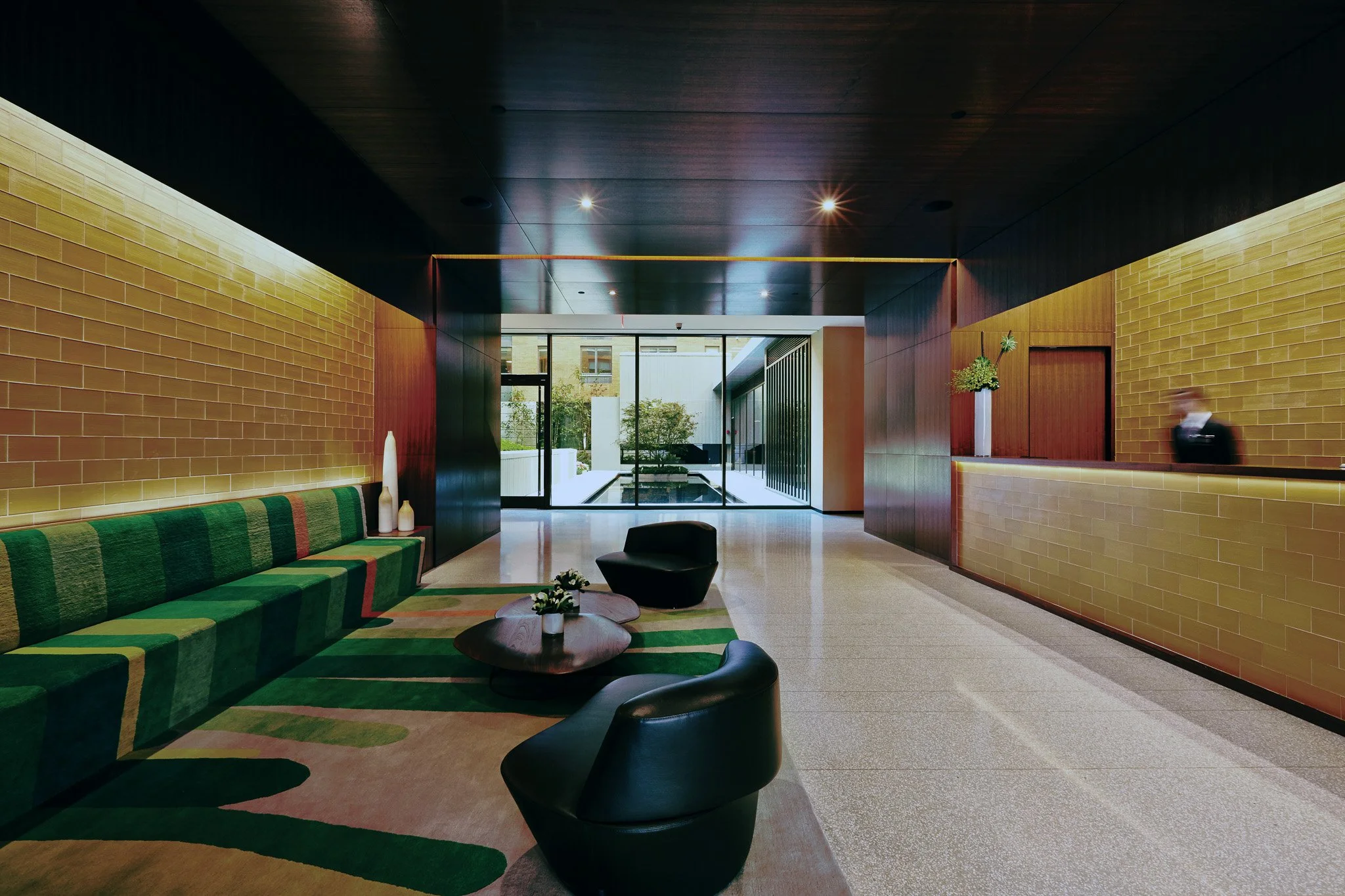 JGNA residential lobby with glazed brick walls, a striped green banquette, sculptural chairs, and a reception desk