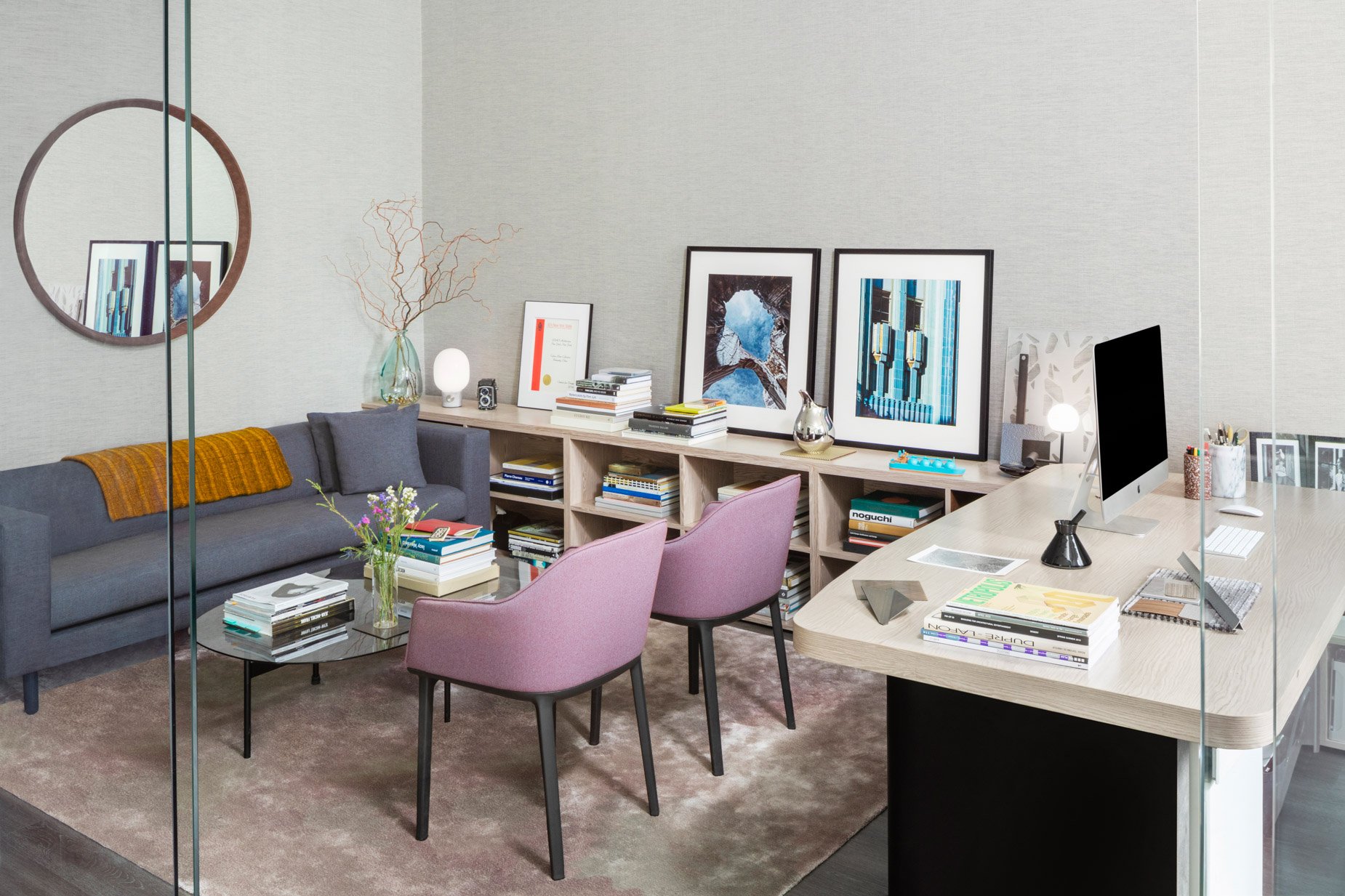 JGNA private office with an oak desk, grey sofa, pink chairs, and framed artwork on a low credenza