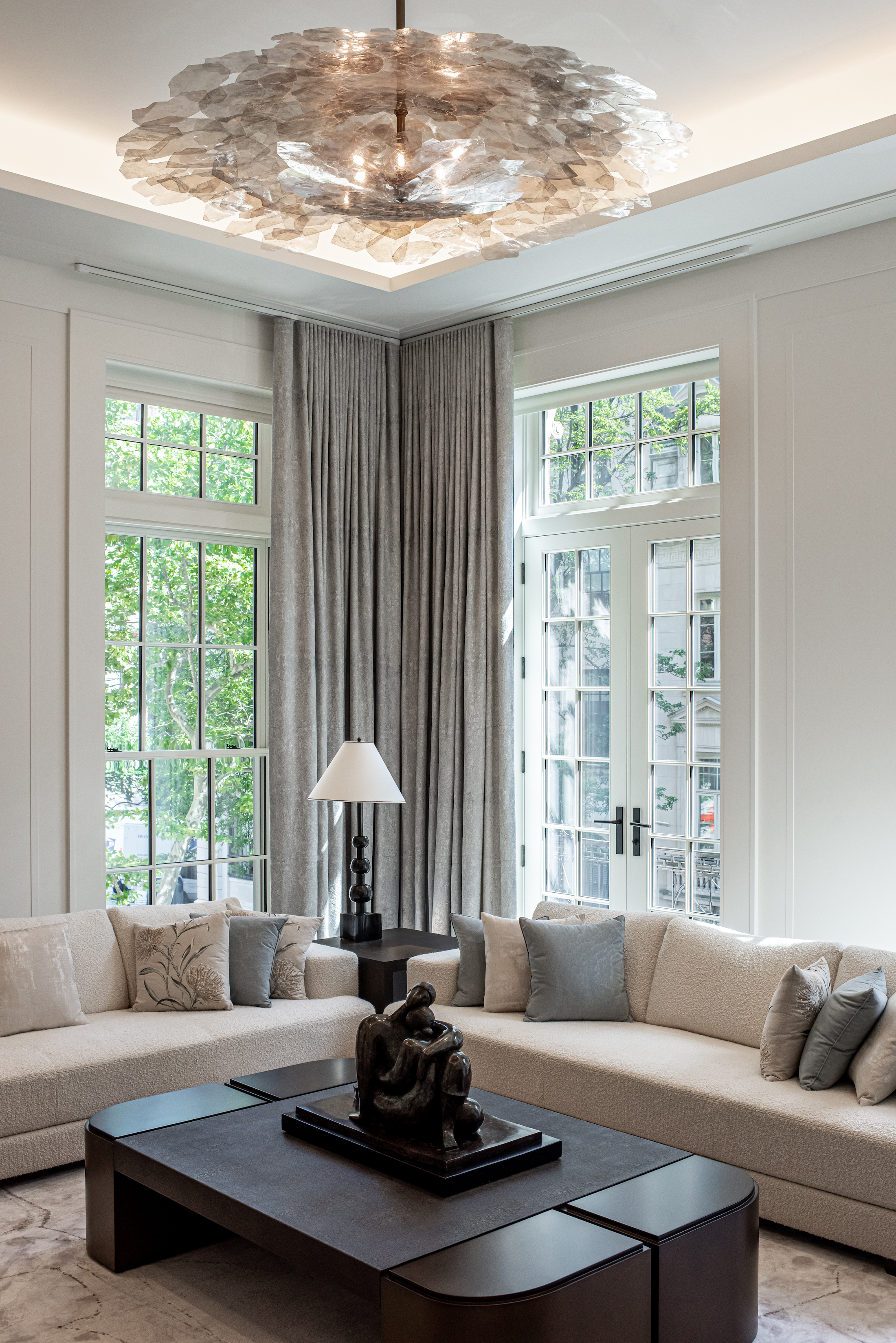 Formal living room with a selenite crystal chandelier, floor-to-ceiling French windows, and cream bouclé sofas