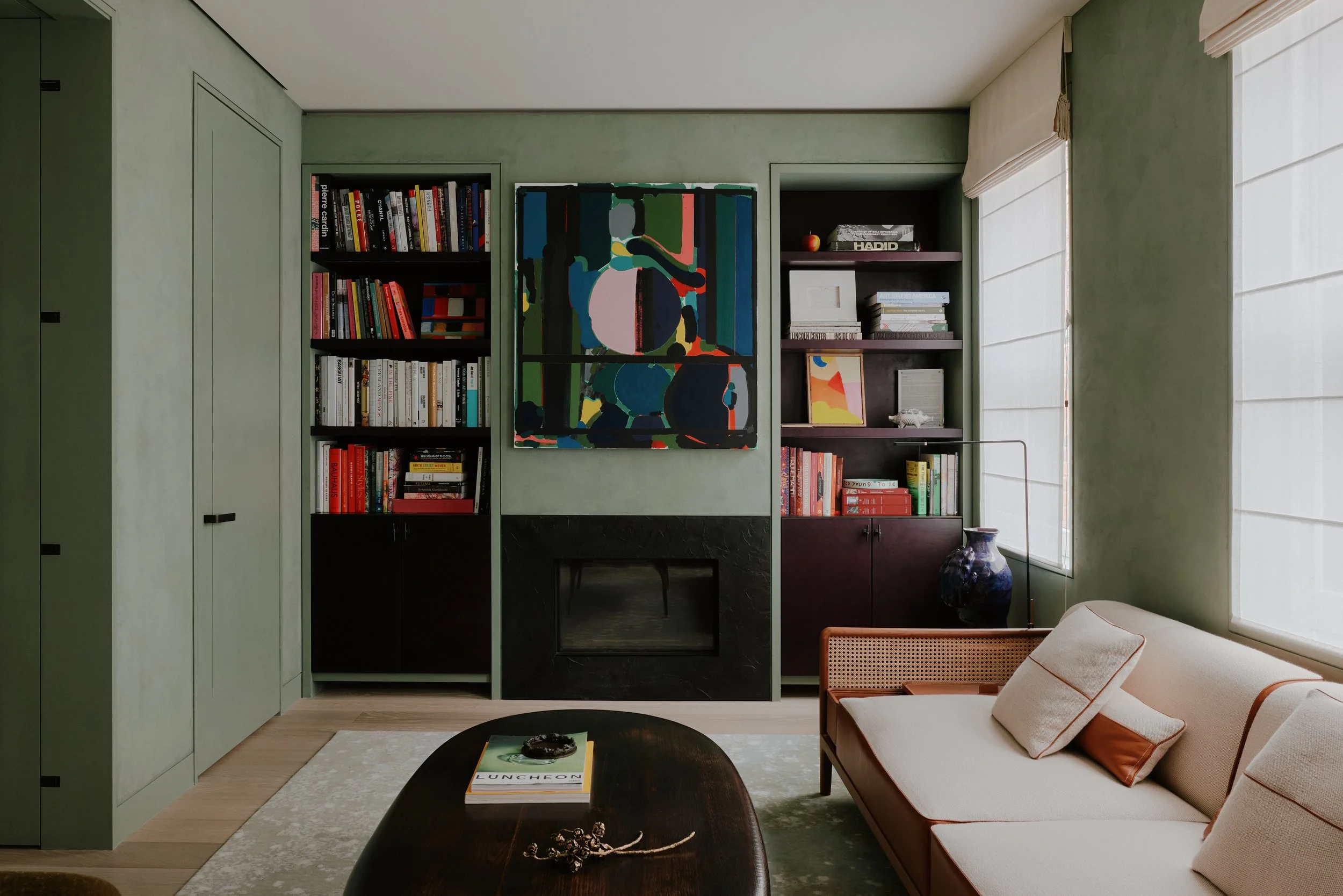 Library with black built-in shelving, a fireplace, and a colorful painting in a West Village townhouse by JG Neukomm Architecture