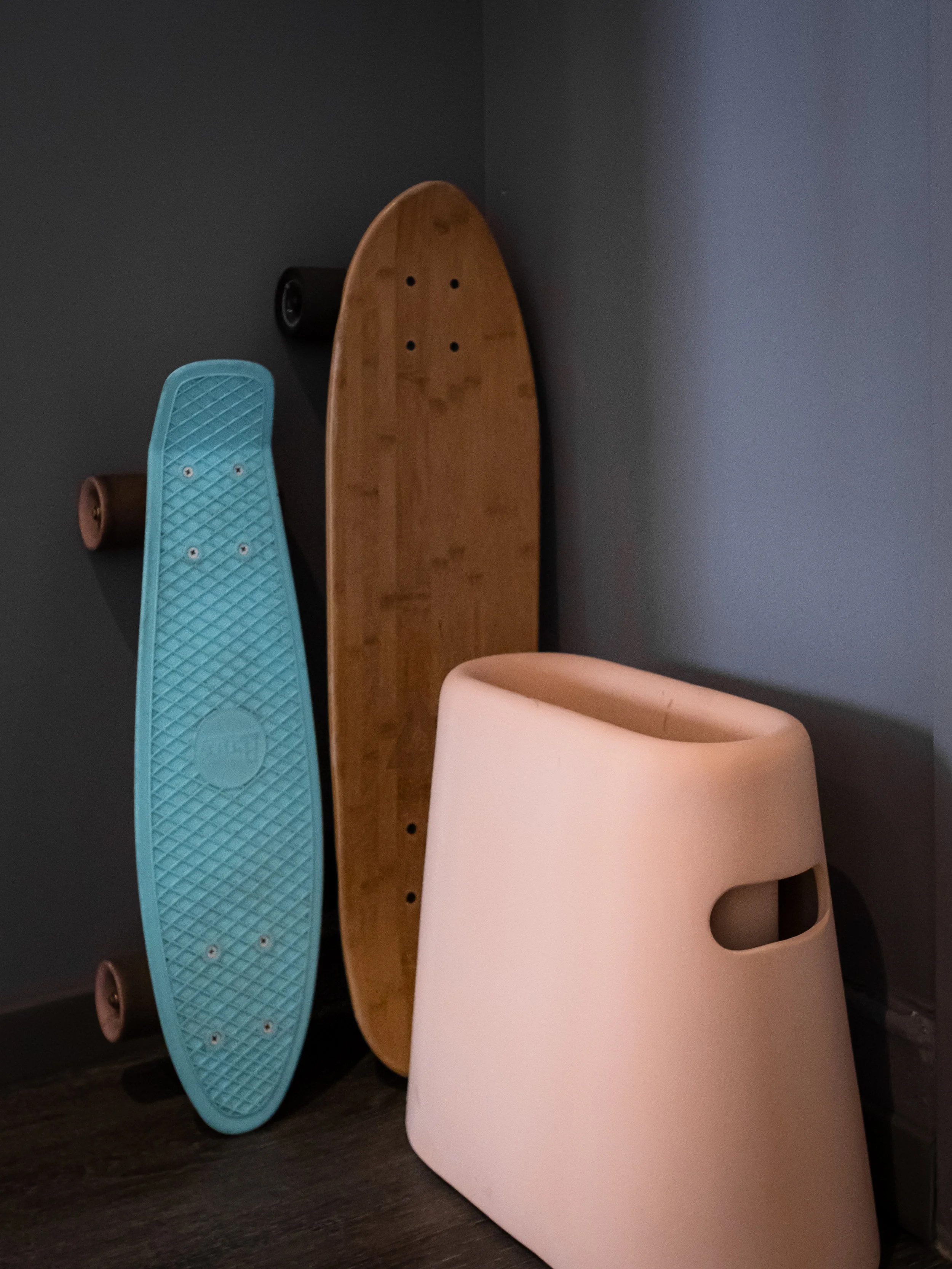JGNA studio corner detail with two skateboards and a molded pink stool against a grey wall
