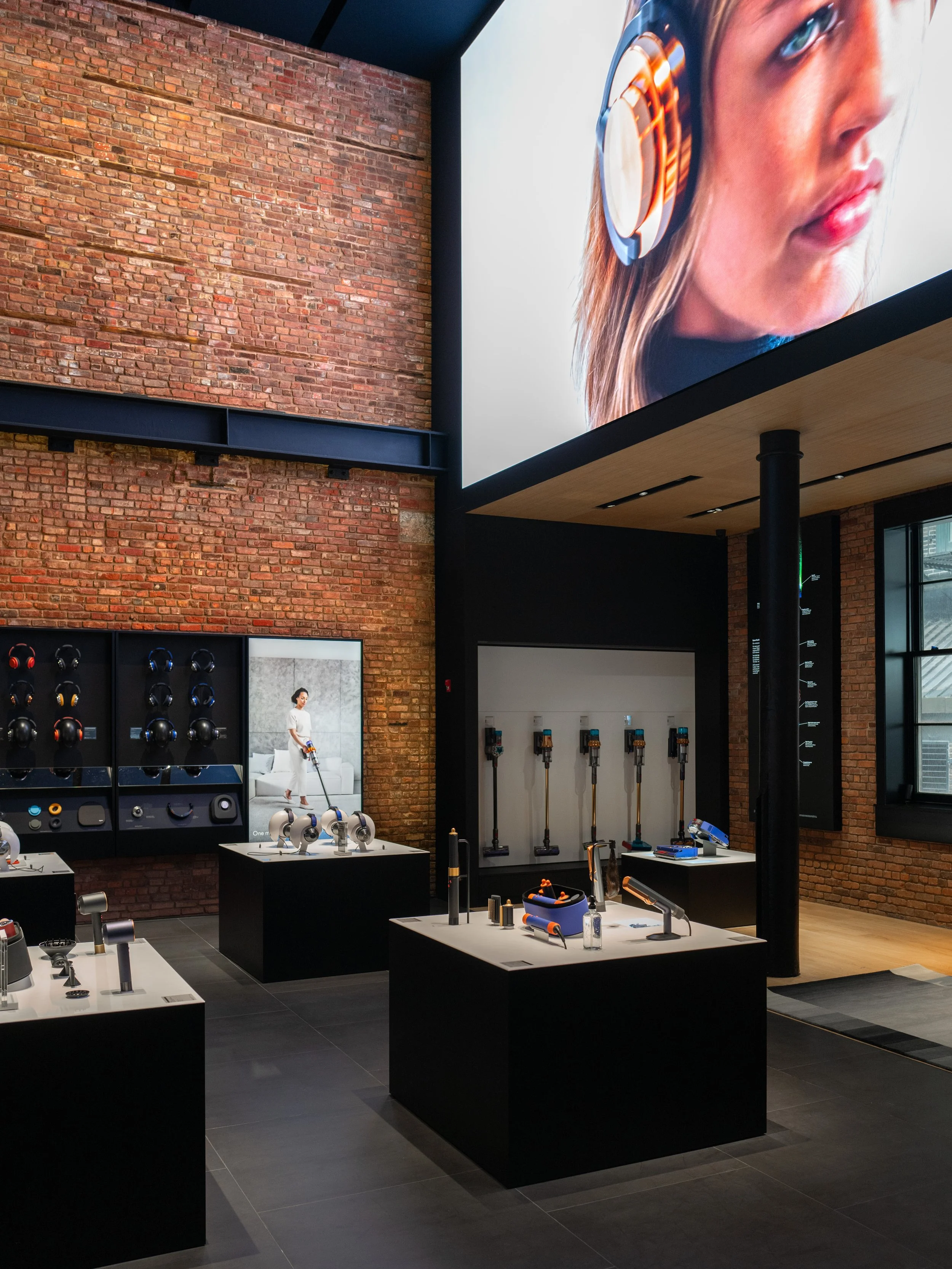 JGNA-designed Dyson Demo Store with exposed brick, a large overhead screen, and black product display plinths