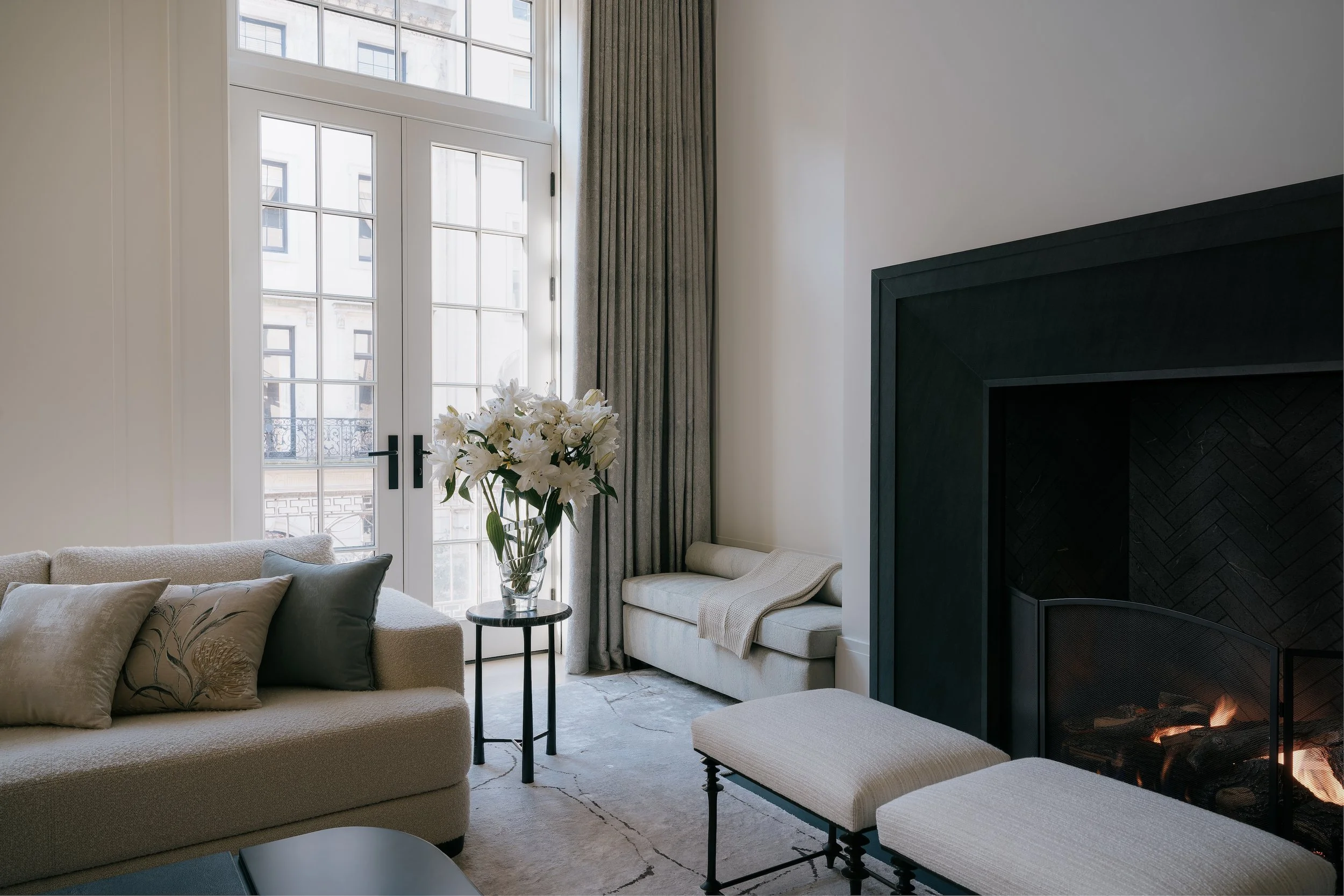 Living room corner with a black-trimmed marble fireplace and French doors overlooking the city