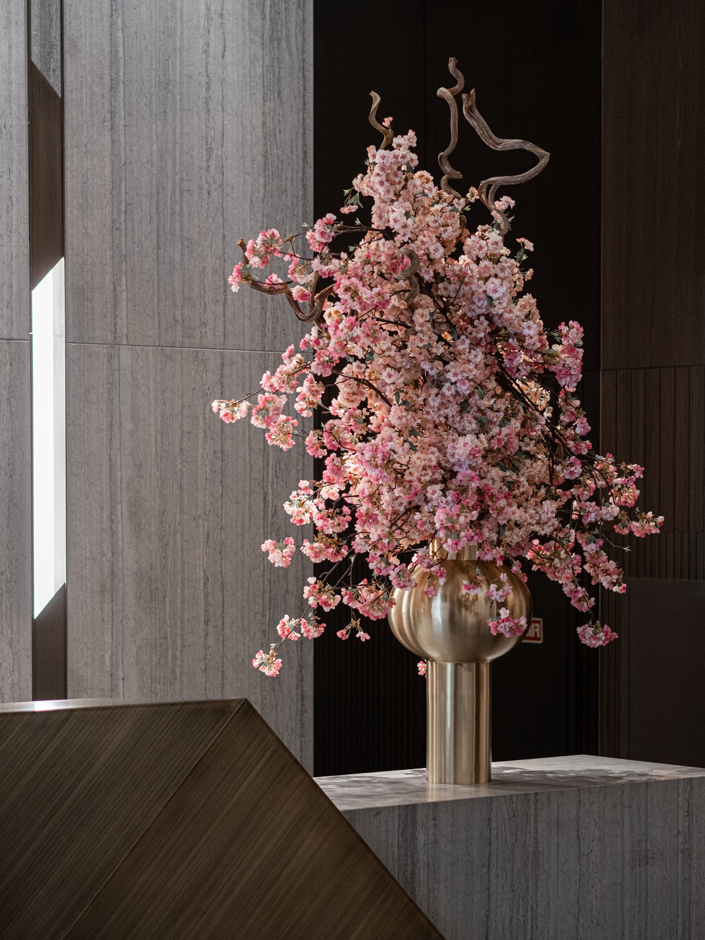 JGNA residential lobby detail of a cherry-blossom arrangement in a brass vase against a travertine wall
