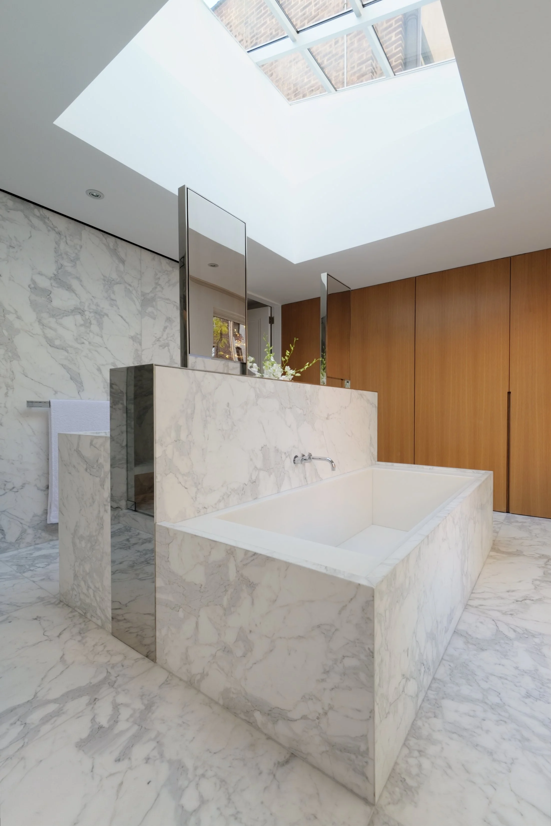 Full marble master bathroom with sculptural freestanding soaking tub, skylight, and warm wood cabinetry in Fabien Baron Residence, West Village NYC by JG Neukomm Architecture