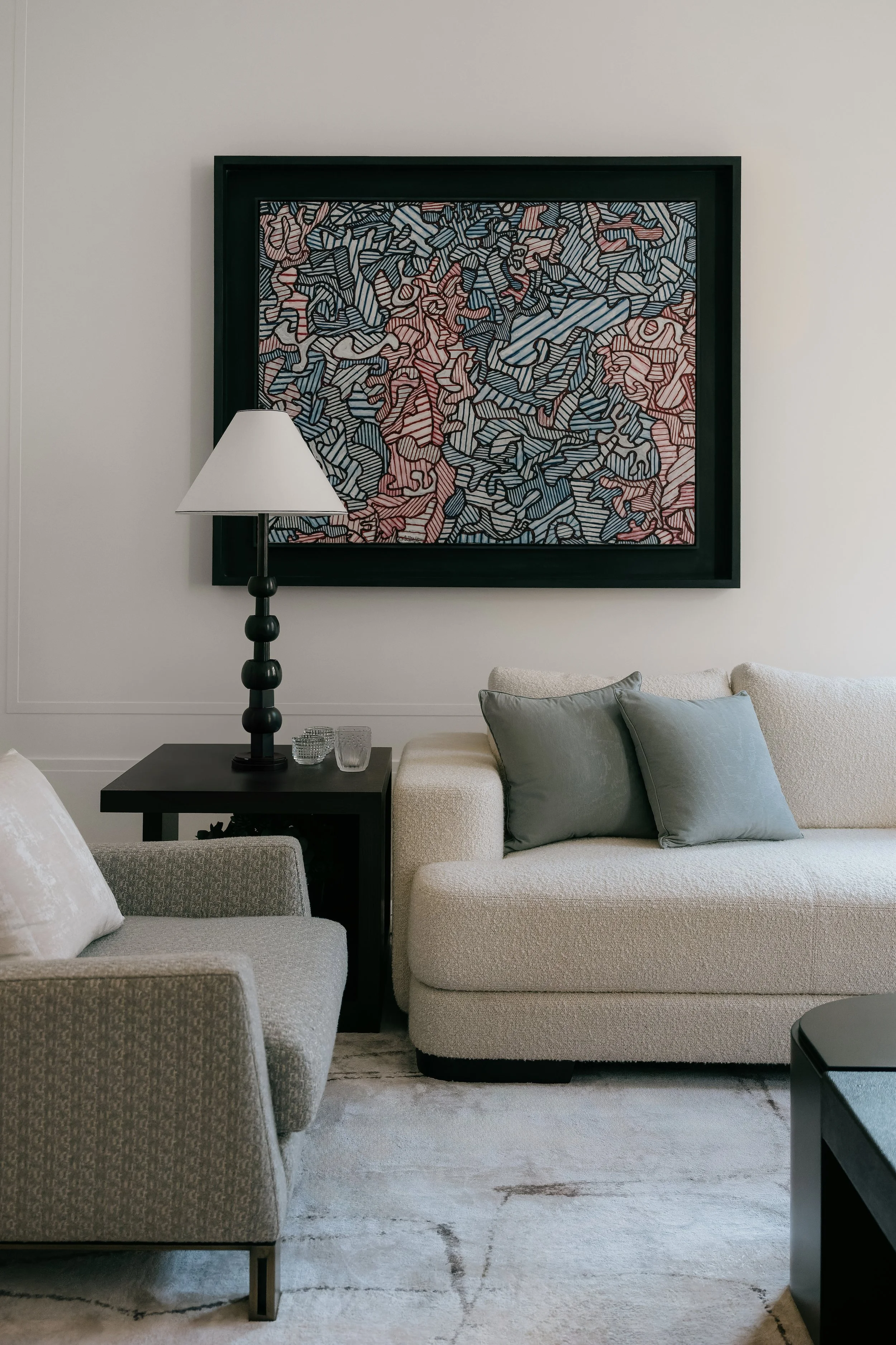 Cozy, modern living room corner in an Upper East Side townhouse featuring a textured cream sofa, grey armchair, abstract wall art, and contemporary lighting designed by JG Neukomm Architecture
