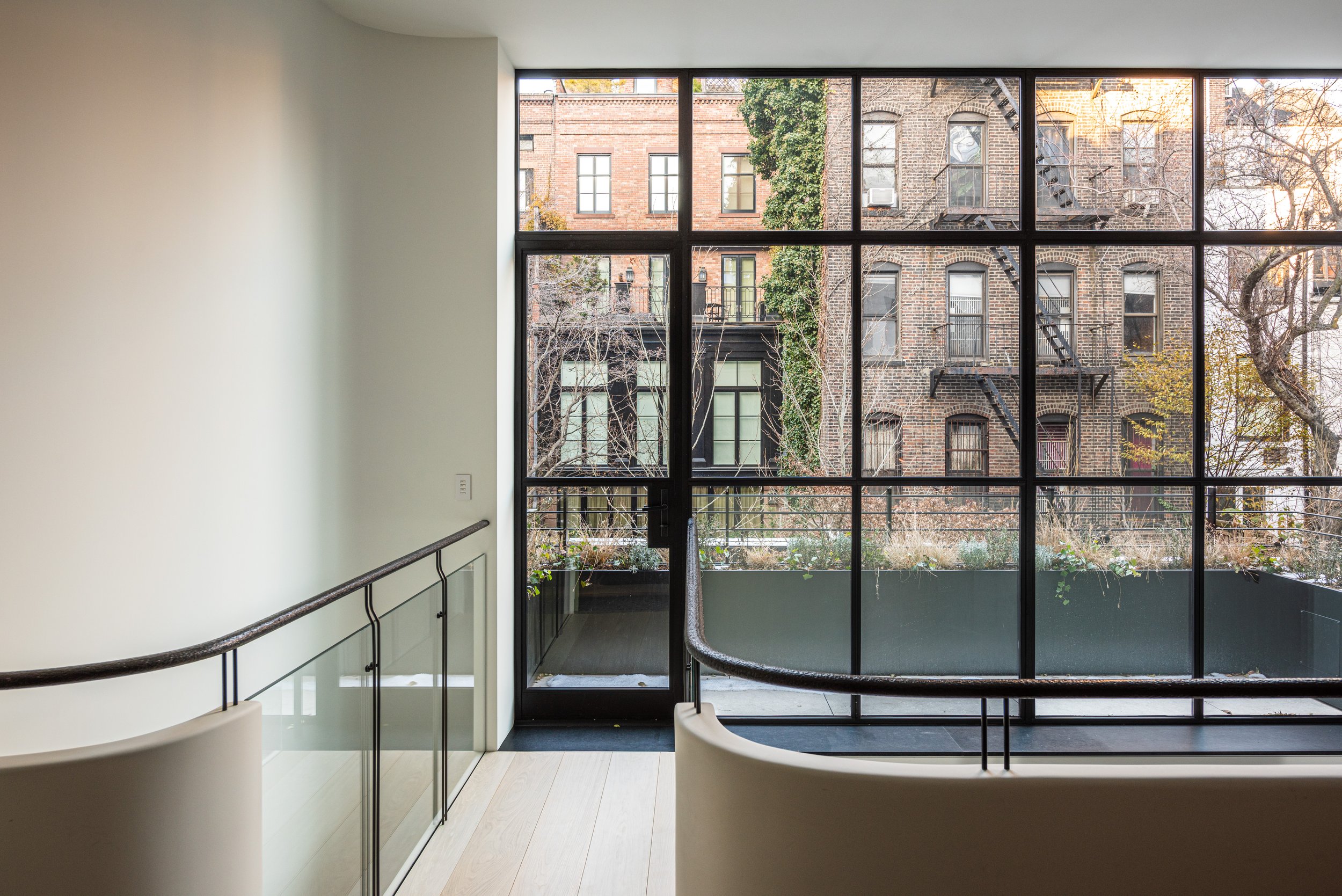 Stair landing with a steel-framed window overlooking West Village townhouses, by JG Neukomm Architecture