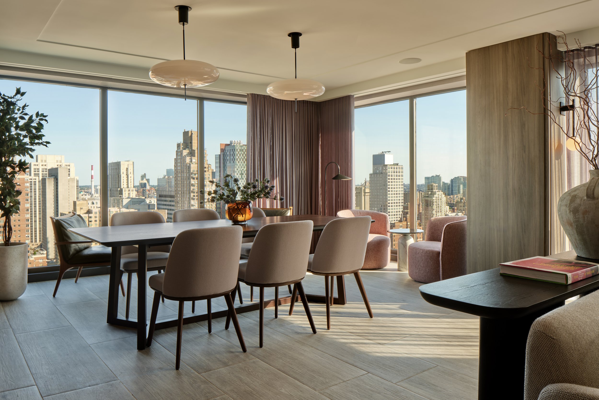 JGNA residential dining and lounge area with a long table, glass globe pendants, and floor-to-ceiling skyline windows