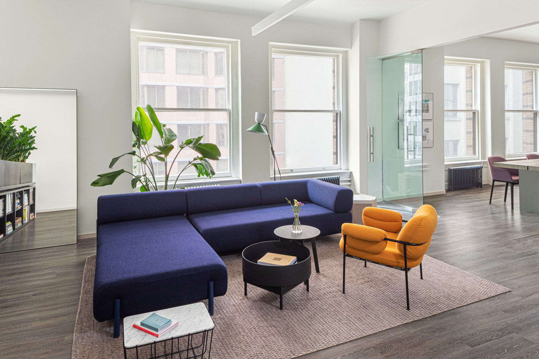 JGNA office lounge with a navy modular sofa, yellow armchair, and round windows overlooking the city