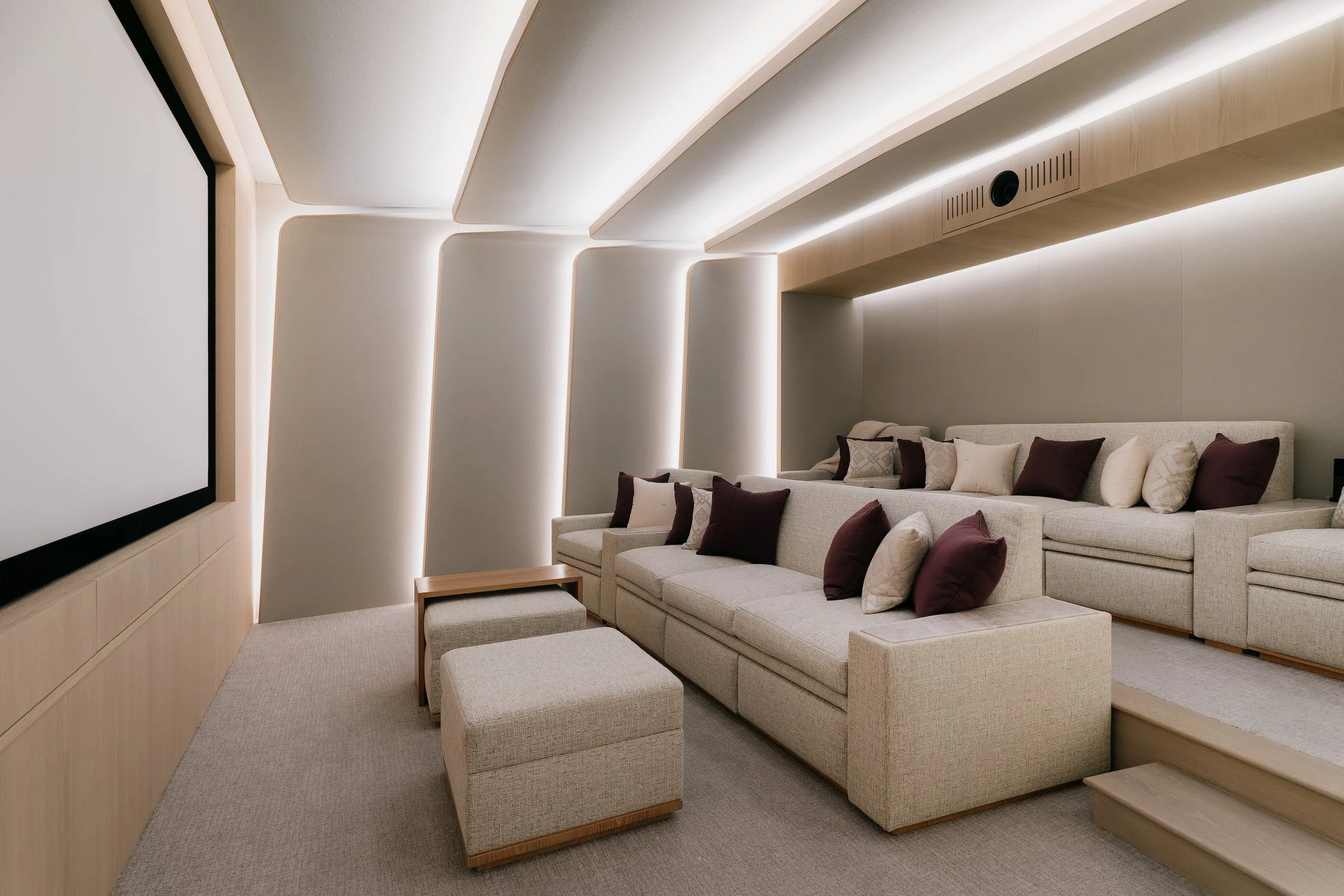 Home theater with tiered sectional seating, a projection screen, and warm cove lighting