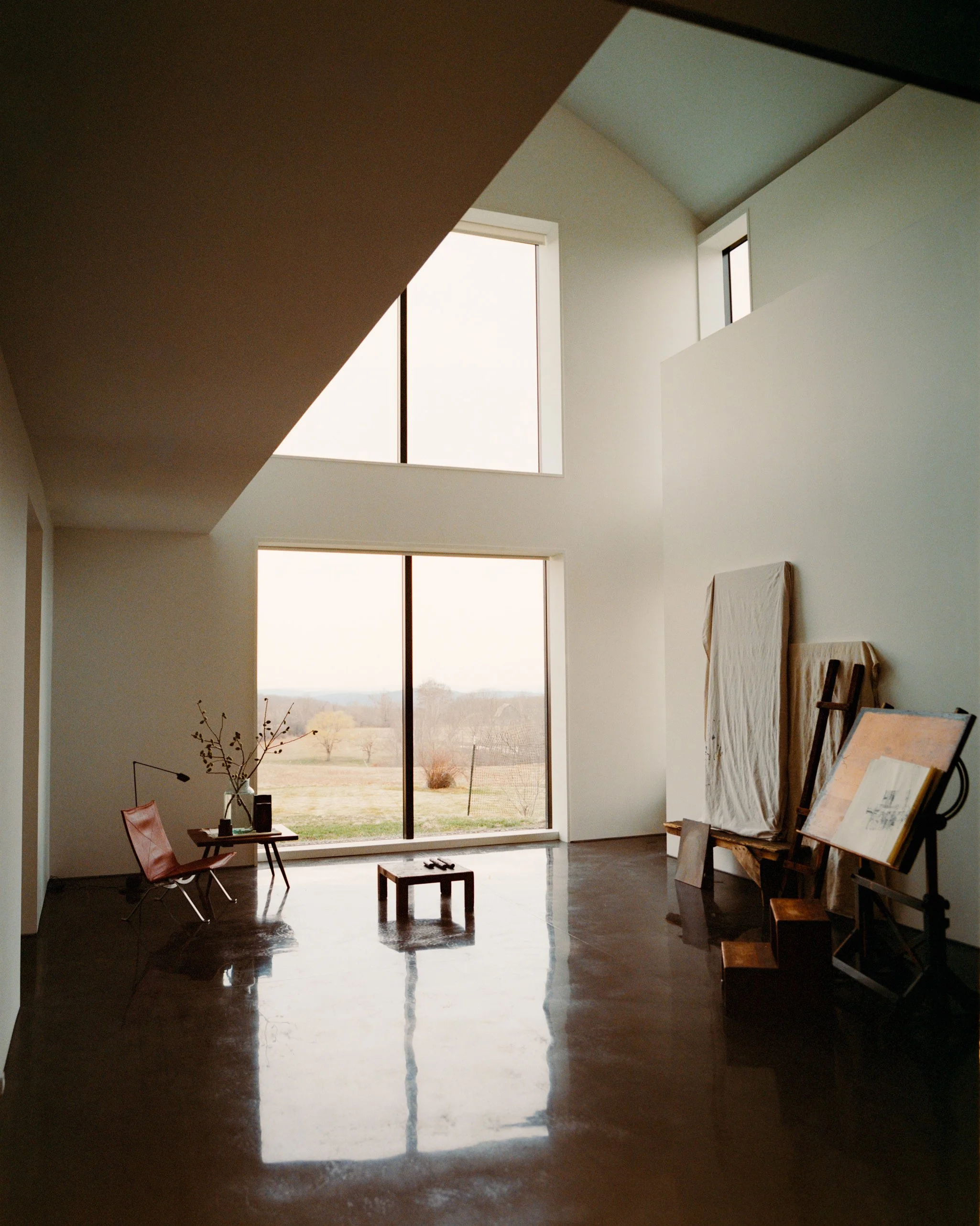Double-height living room with polished concrete floors and tall windows overlooking the countryside in a Ghent, NY home by JG Neukomm Architecture