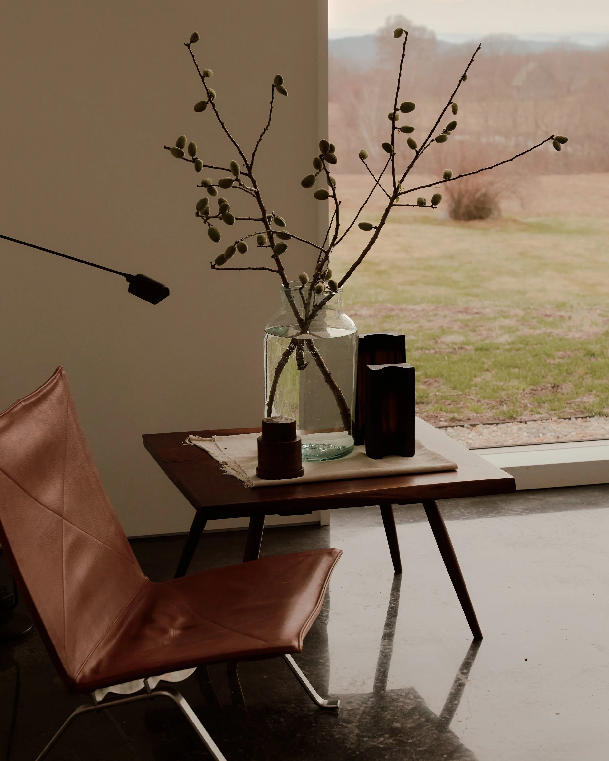 Leather sling chair and wood side table beside a window framing the countryside at a Ghent, NY home by JG Neukomm Architecture