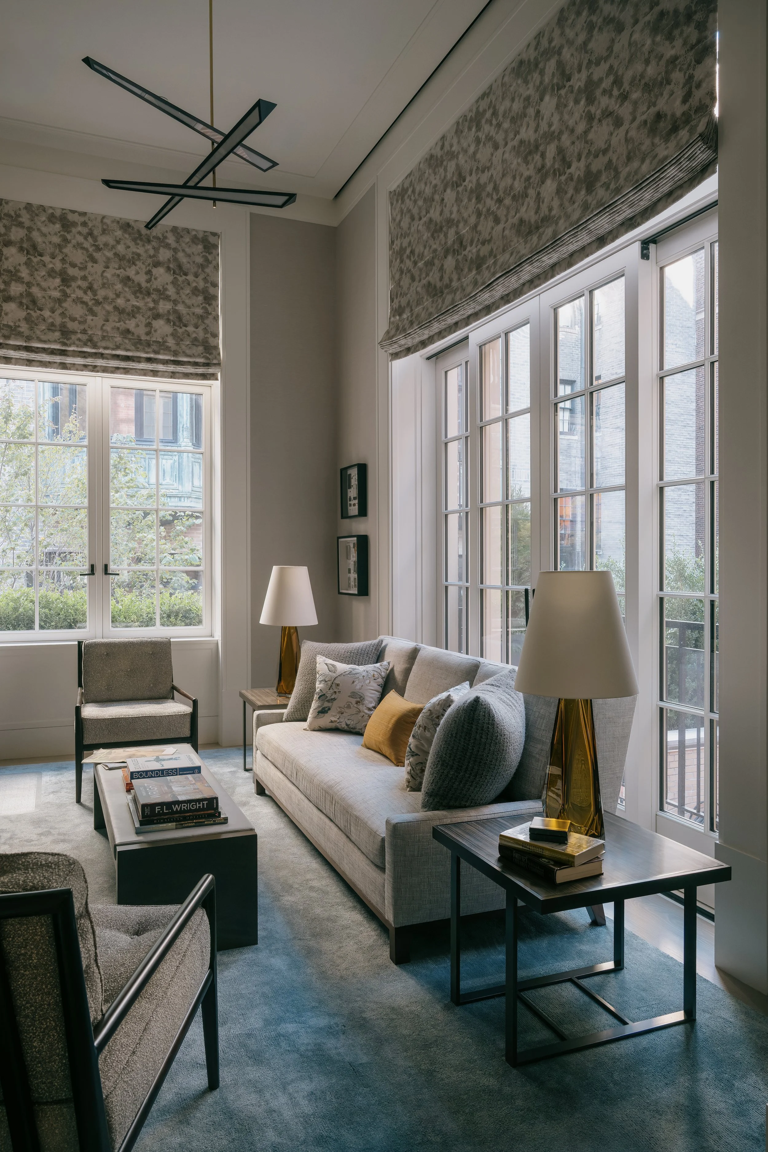 Sitting room with a geometric black tube chandelier, patterned roman shades, and grey sofa