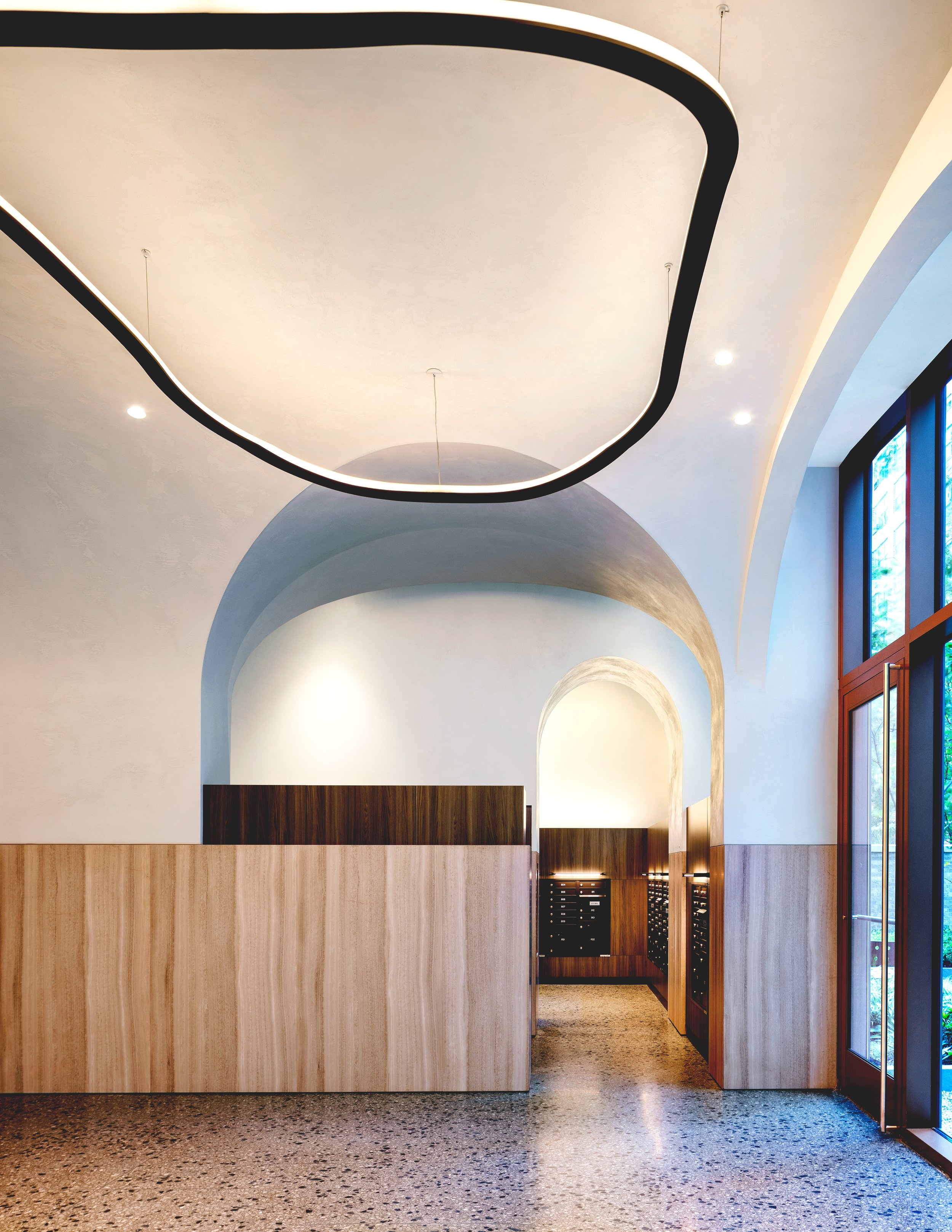 Lobby with a sculptural arched plaster ceiling and illuminated ring pendants at The Suffolk, a Lower East Side residential building, interiors by JG Neukomm Architecture