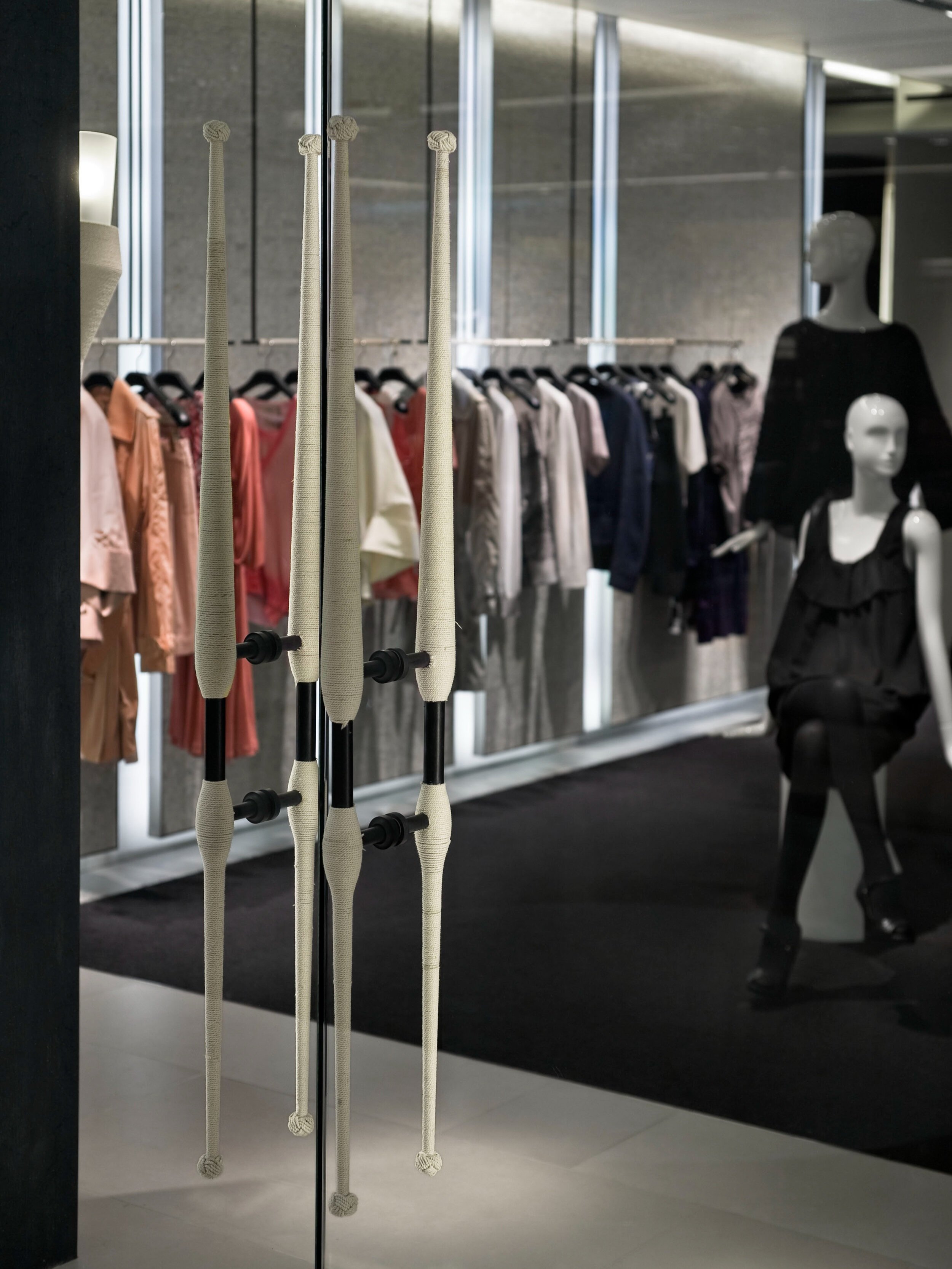 JGNA boutique interior with rope-wrapped vertical columns, a garment rail, and a black-clad mannequin on dark carpet