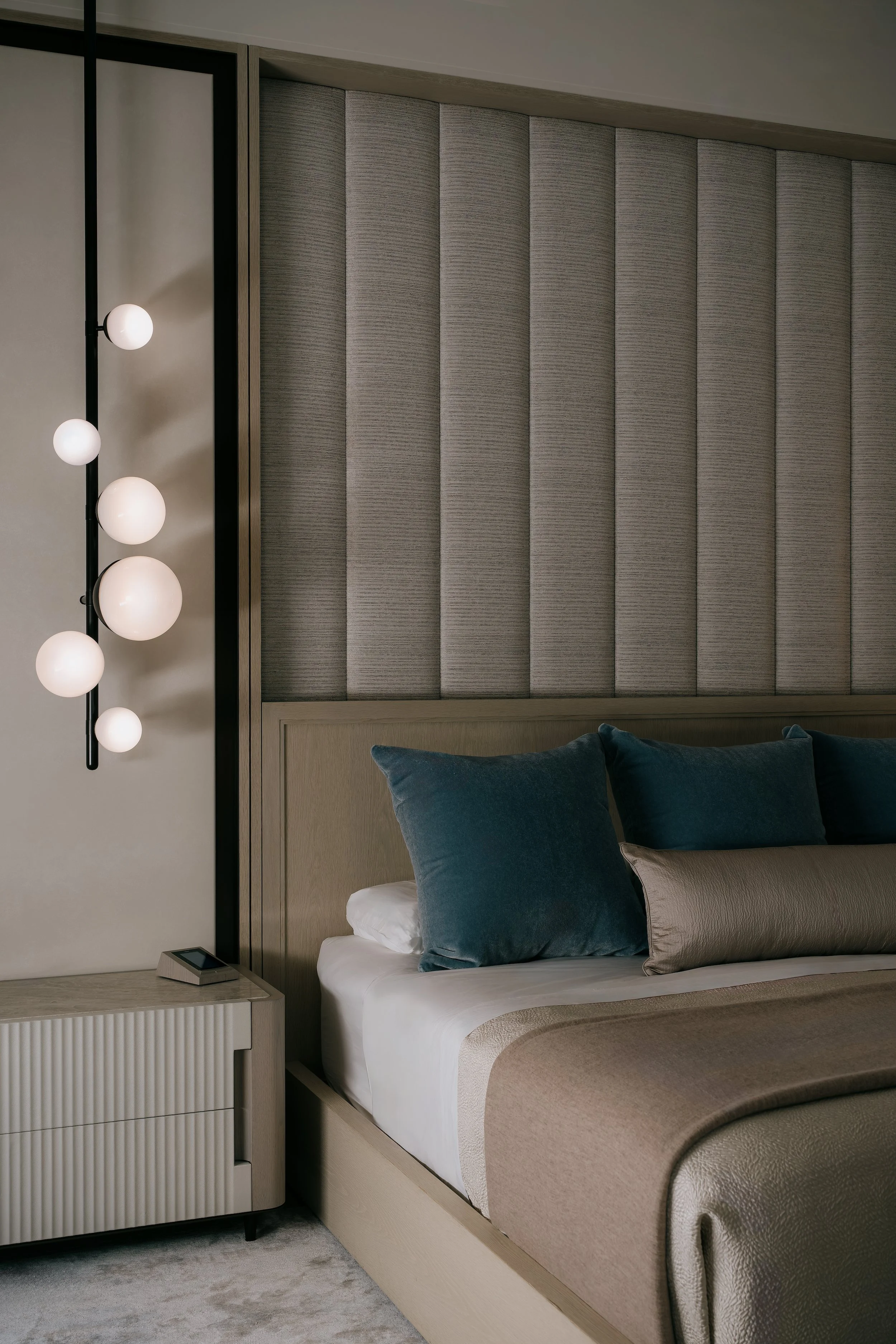 Detail of cascading glass globe pendants beside a channel-tufted upholstered headboard