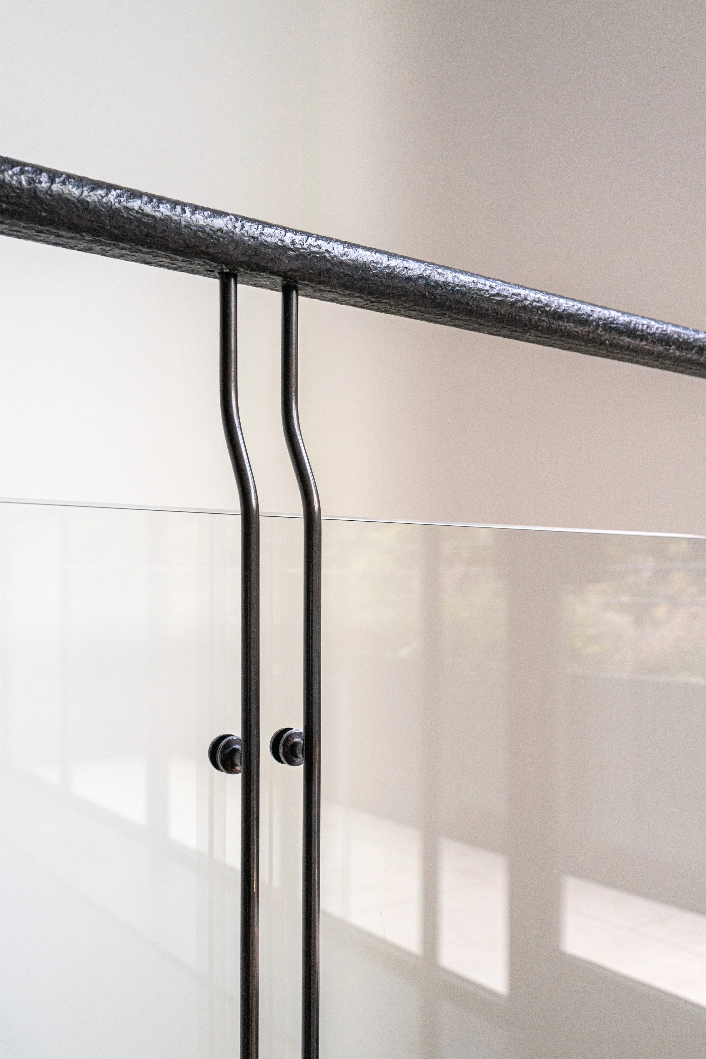 Stair landing with a glass balustrade and a curved black handrail in a West Village townhouse by JG Neukomm Architecture