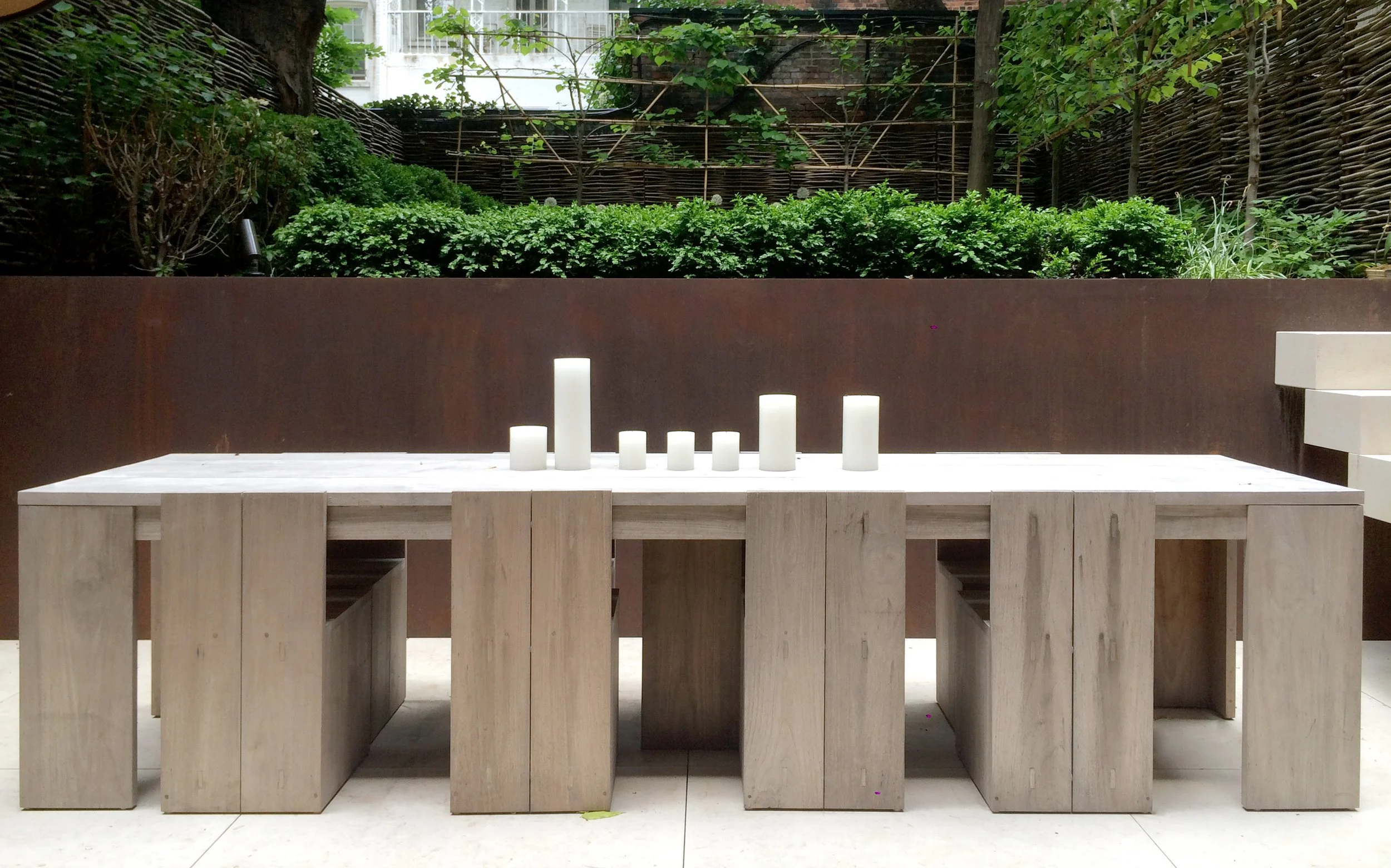 Outdoor dining area with weathered oak table, bench seating, pillar candles, and Corten steel wall in Fabien Baron's West Village townhouse garden by JG Neukomm Architecture