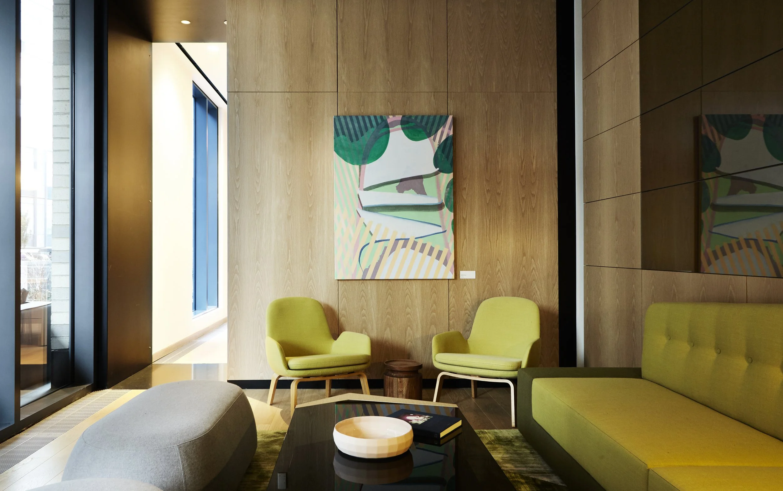 JGNA residential lounge with chartreuse armchairs and banquette, oak paneling, and an abstract painting
