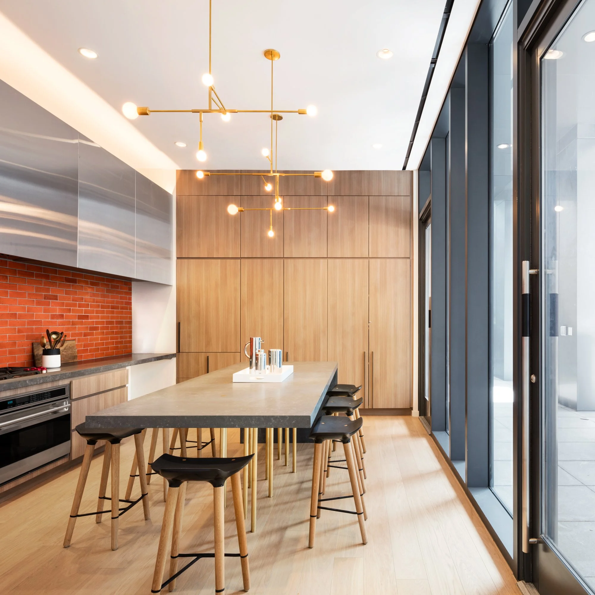 JGNA residential private dining kitchen with an oak table, brass sputnik chandelier, and an orange brick backsplash