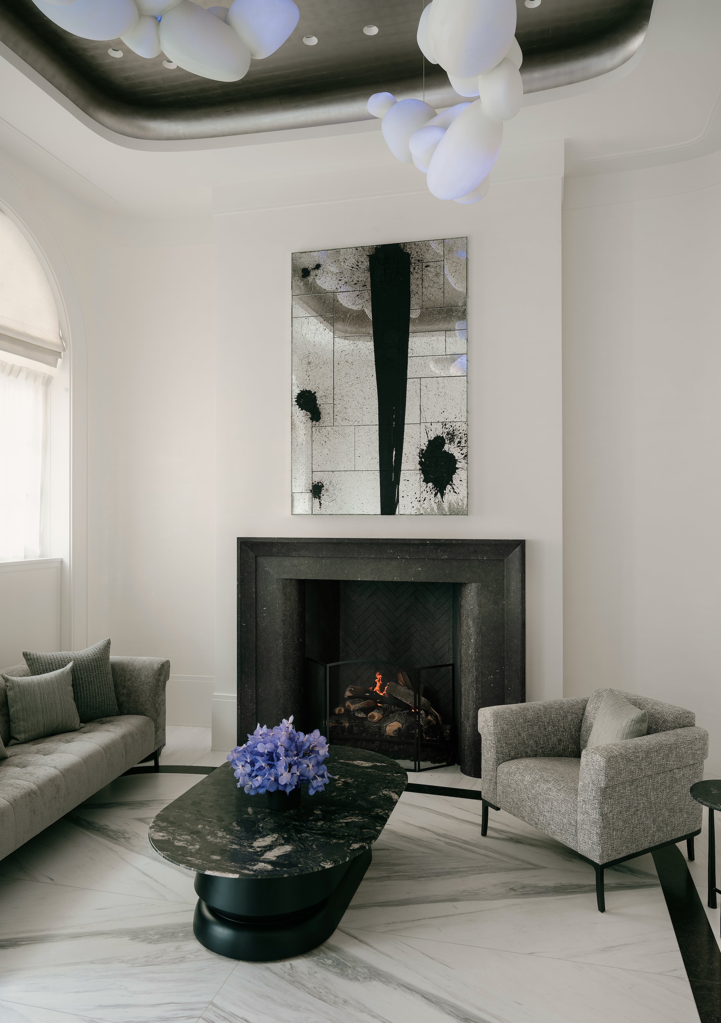 Elegant sitting area with a dark statement fireplace, patterned marble flooring, and sophisticated modern grey furniture in a luxury New York residential design