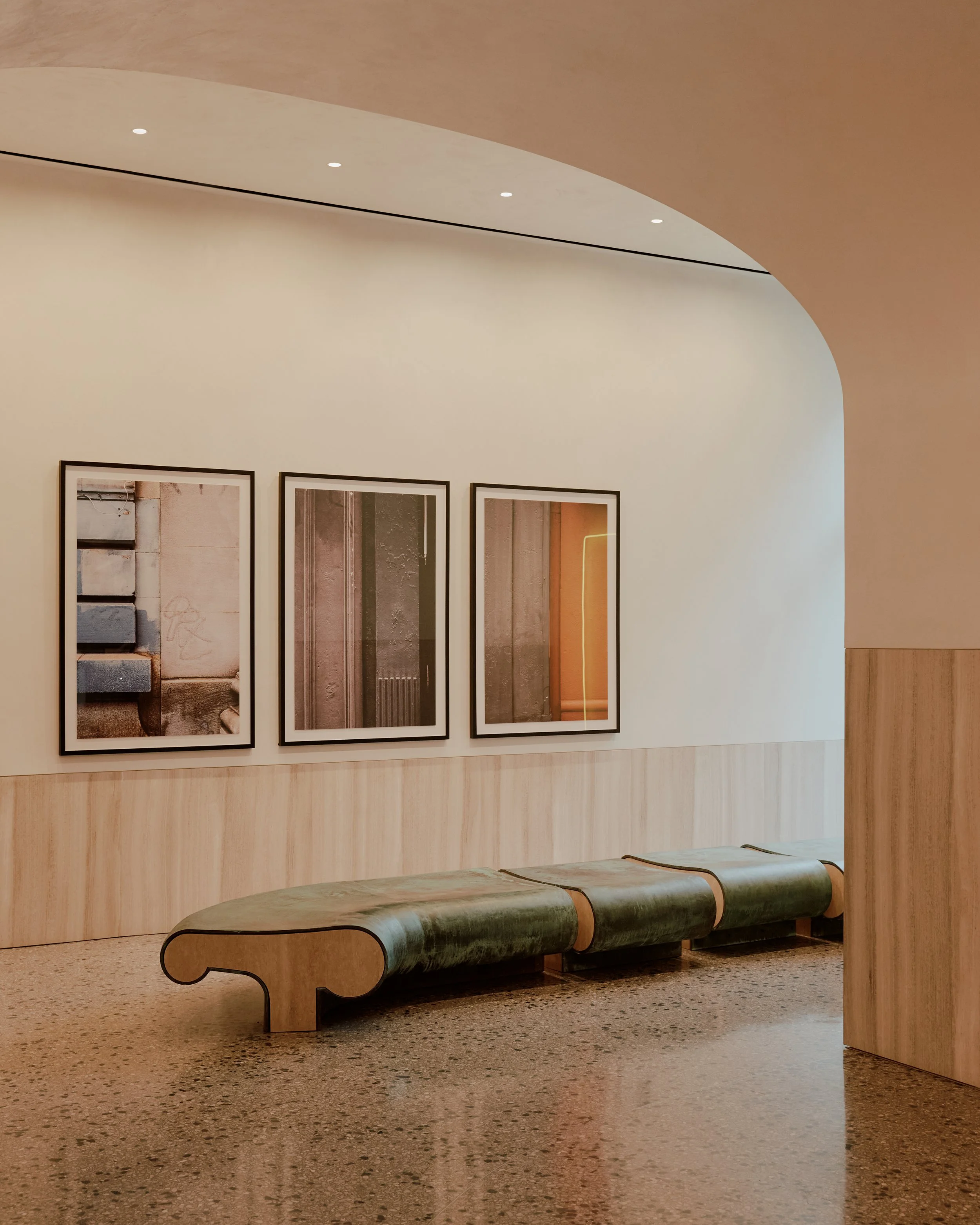 The Suffolk by JGNA featuring a vaulted lobby, custom curved bench seating, framed artwork, terrazzo flooring, and warm wood paneling in New York City's Lower East Side