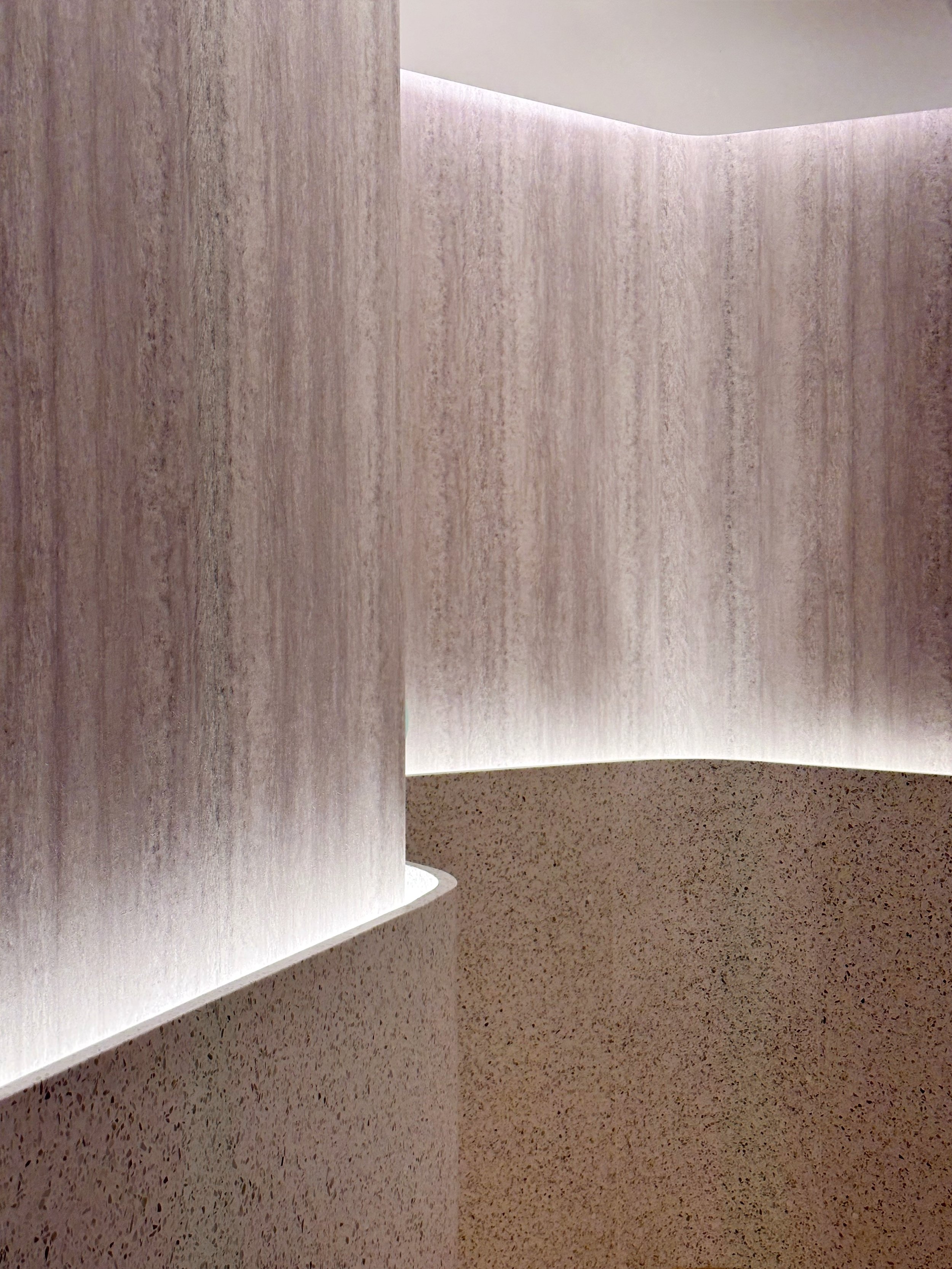 JGNA residential meditation room detail of a curved travertine column and terrazzo base lit by a cove strip