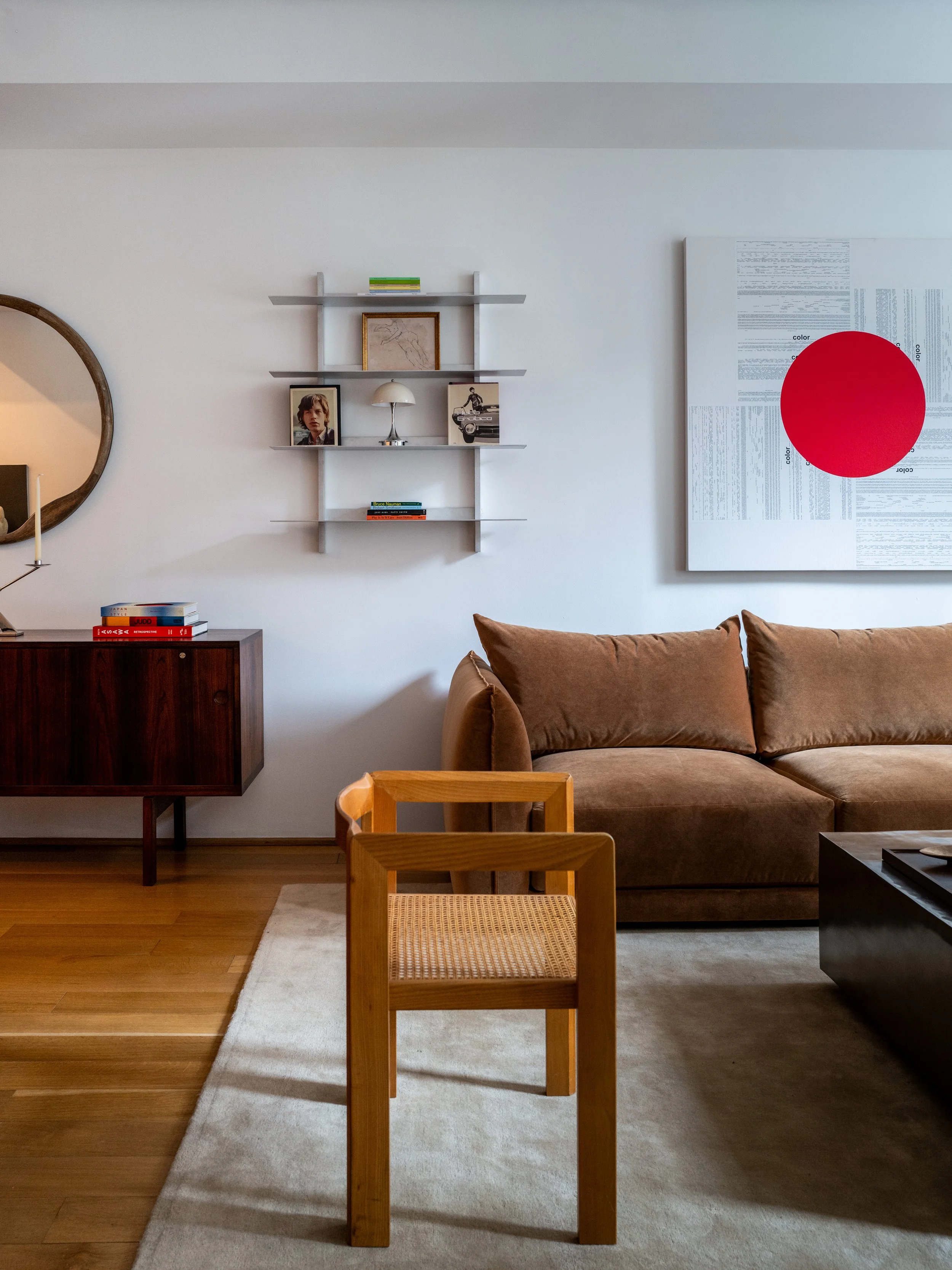 Residential living room with rosewood credenza, wall-mounted metal shelving, round mirror, and oak flooring