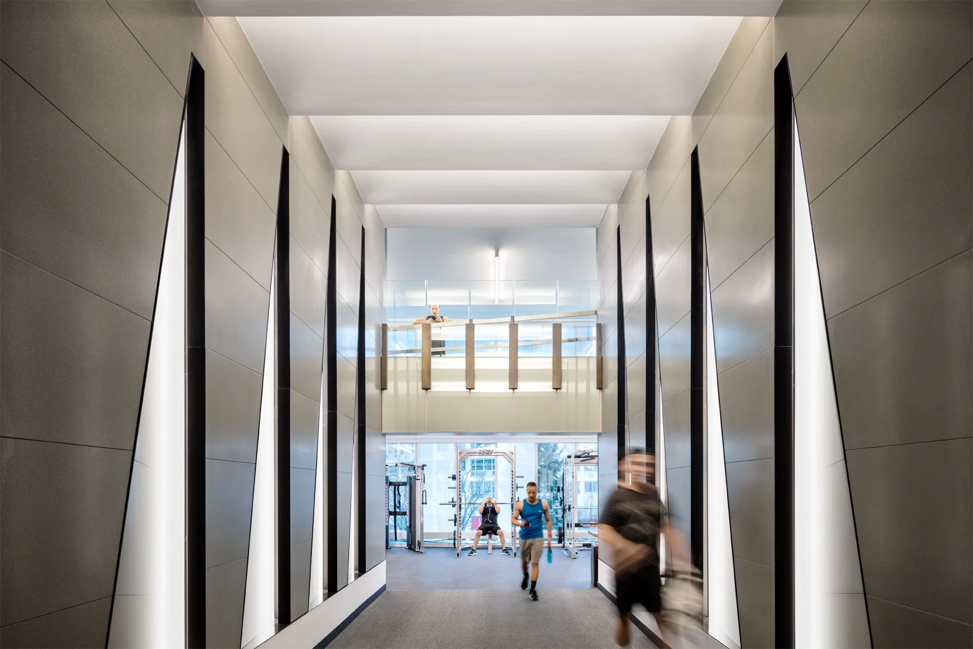 JGNA residential corridor with faceted mirrored walls leading toward a fitness room with people in motion