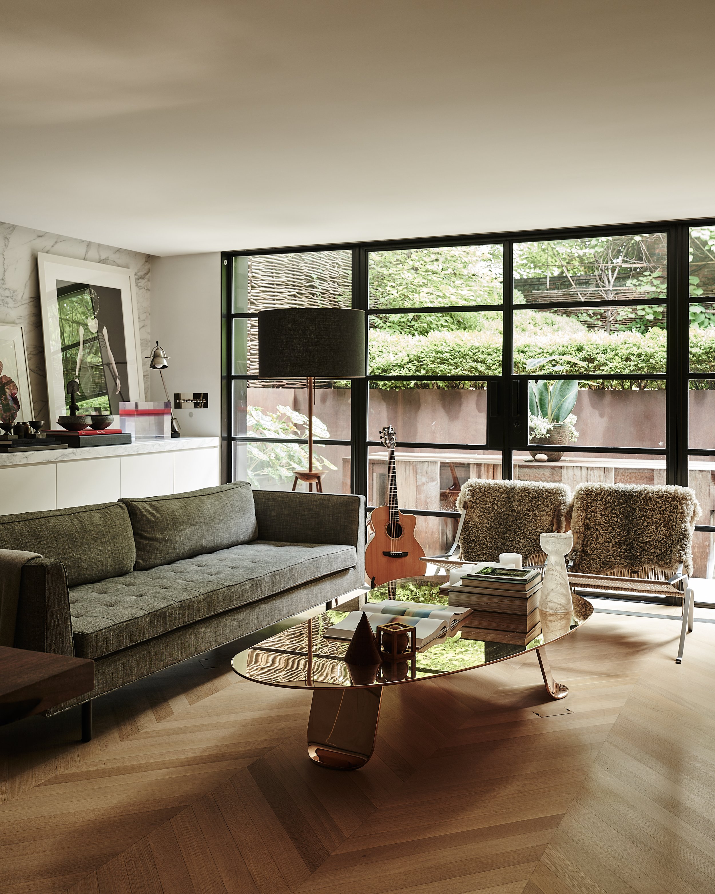 Garden-facing living room with floor-to-ceiling steel-framed windows, tufted sofa, and brass coffee table in Fabien Baron Residence, West Village NYC by JG Neukomm Architecture