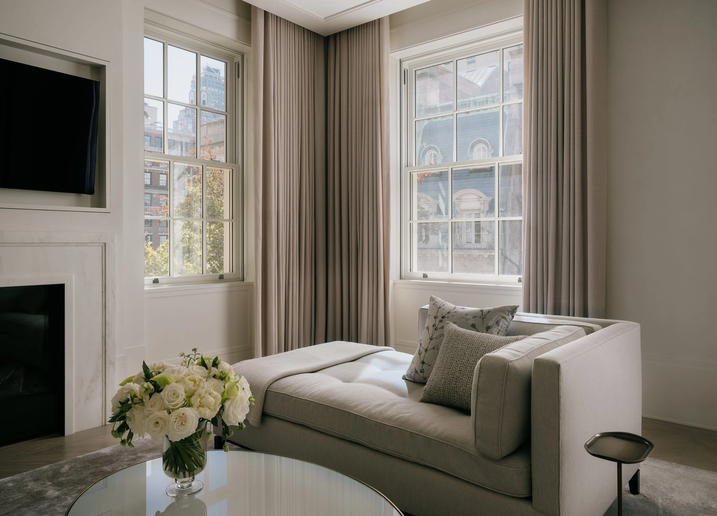 Sitting room with a linen chaise lounge, marble fireplace, and divided-light windows over the city