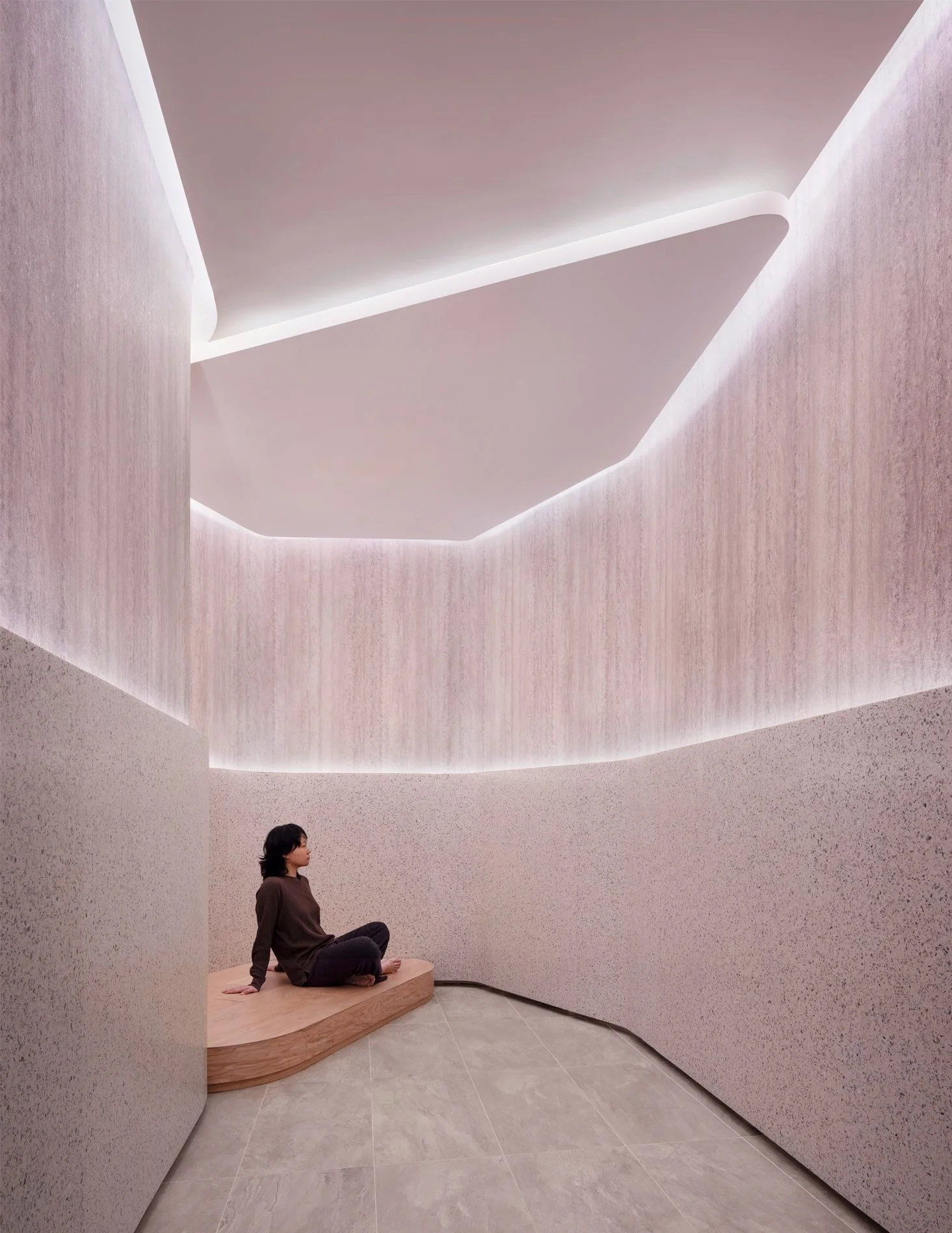 GNA residential meditation room with curved travertine walls, a terrazzo base, hidden cove lighting, and a seated figure