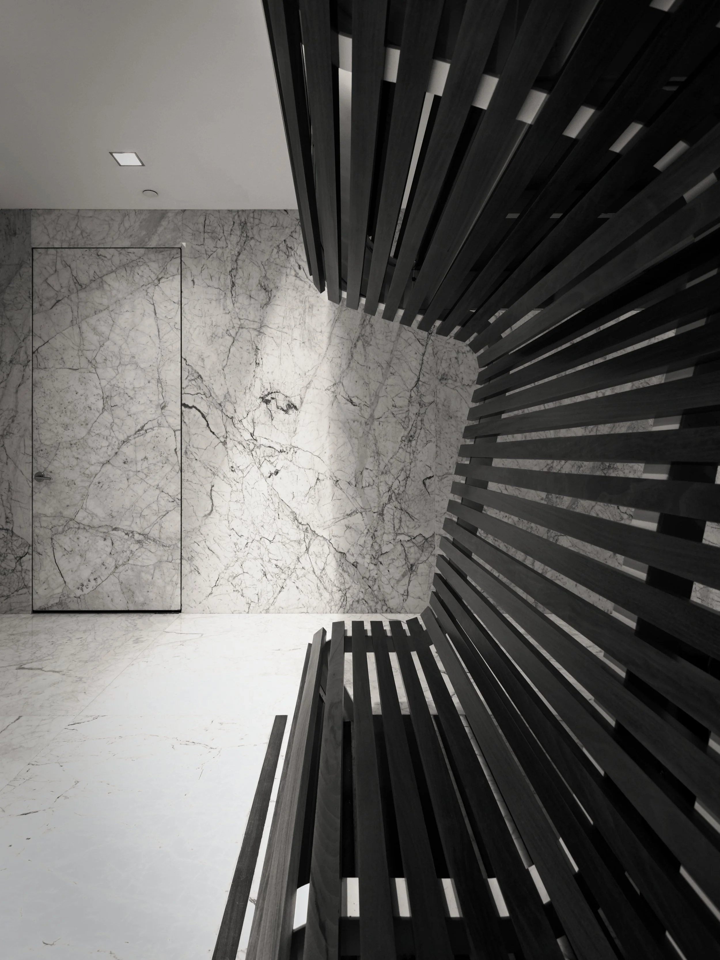 JGNA spa detail of a black wood-slat sculptural bench meeting a marble floor and wall