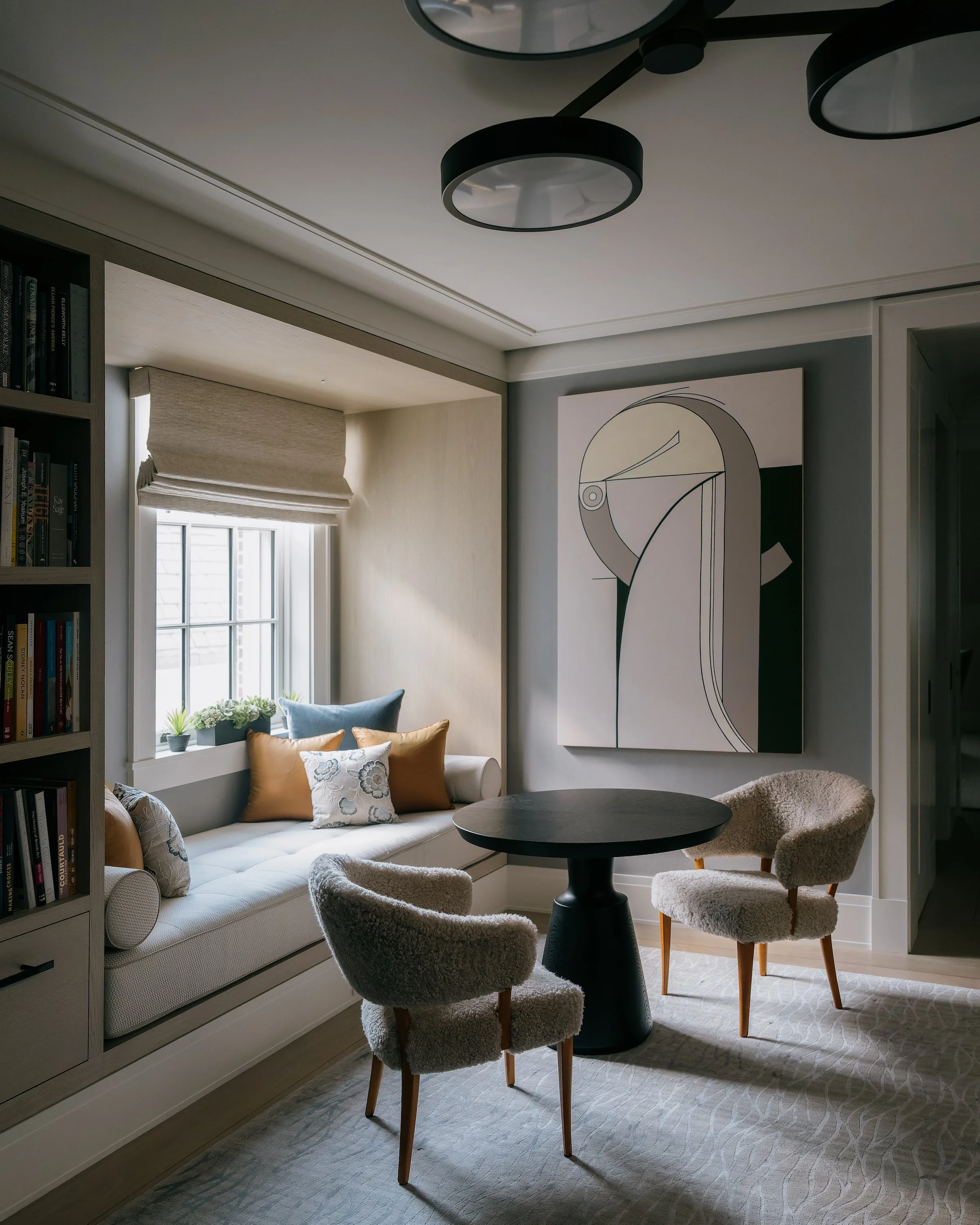Built-in window seat nook with shearling chairs, a pedestal table, and abstract wall art