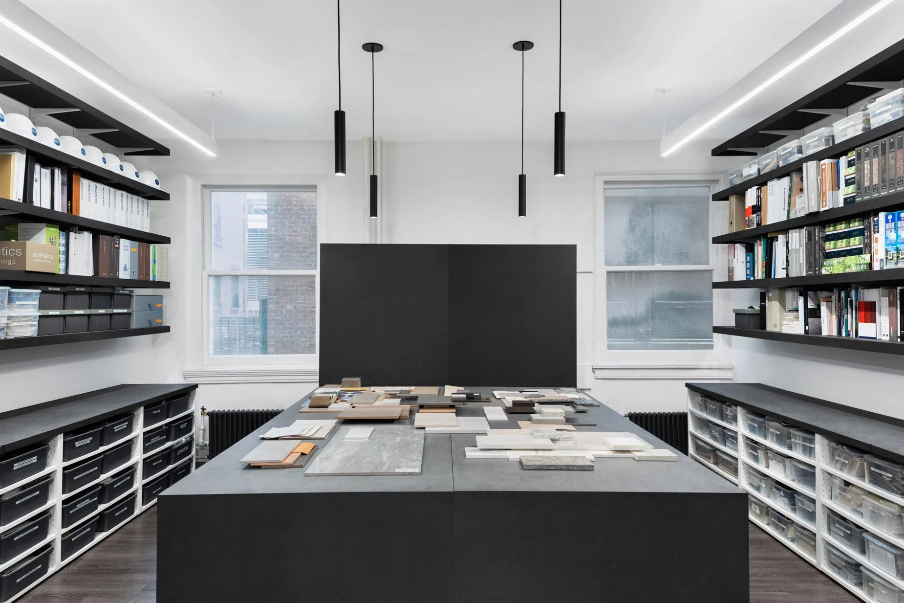 JGNA materials library with samples laid out on a large black table flanked by floor-to-ceiling shelving