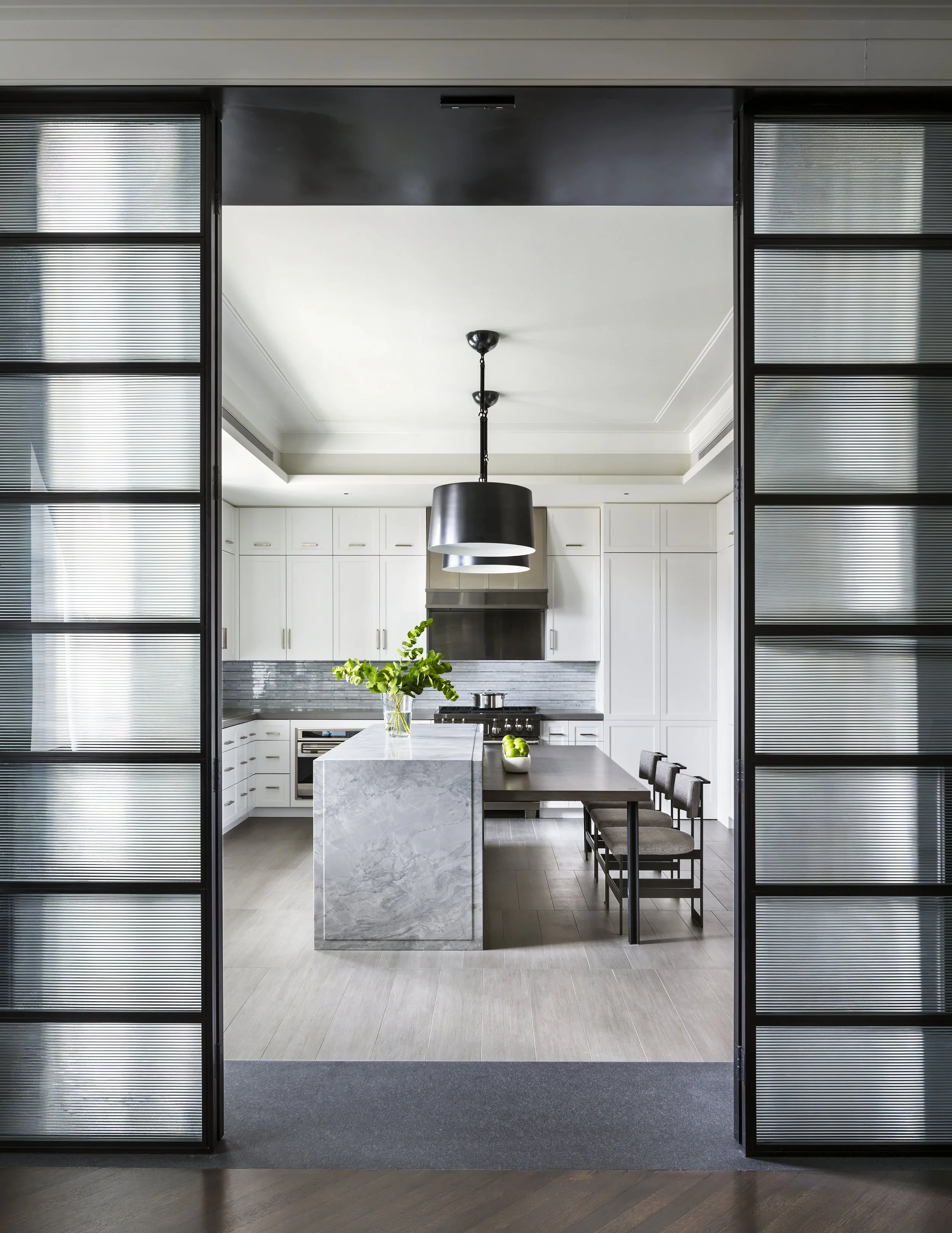 JGNA residence kitchen viewed through fluted-glass sliding doors, with a marble island and drum pendant