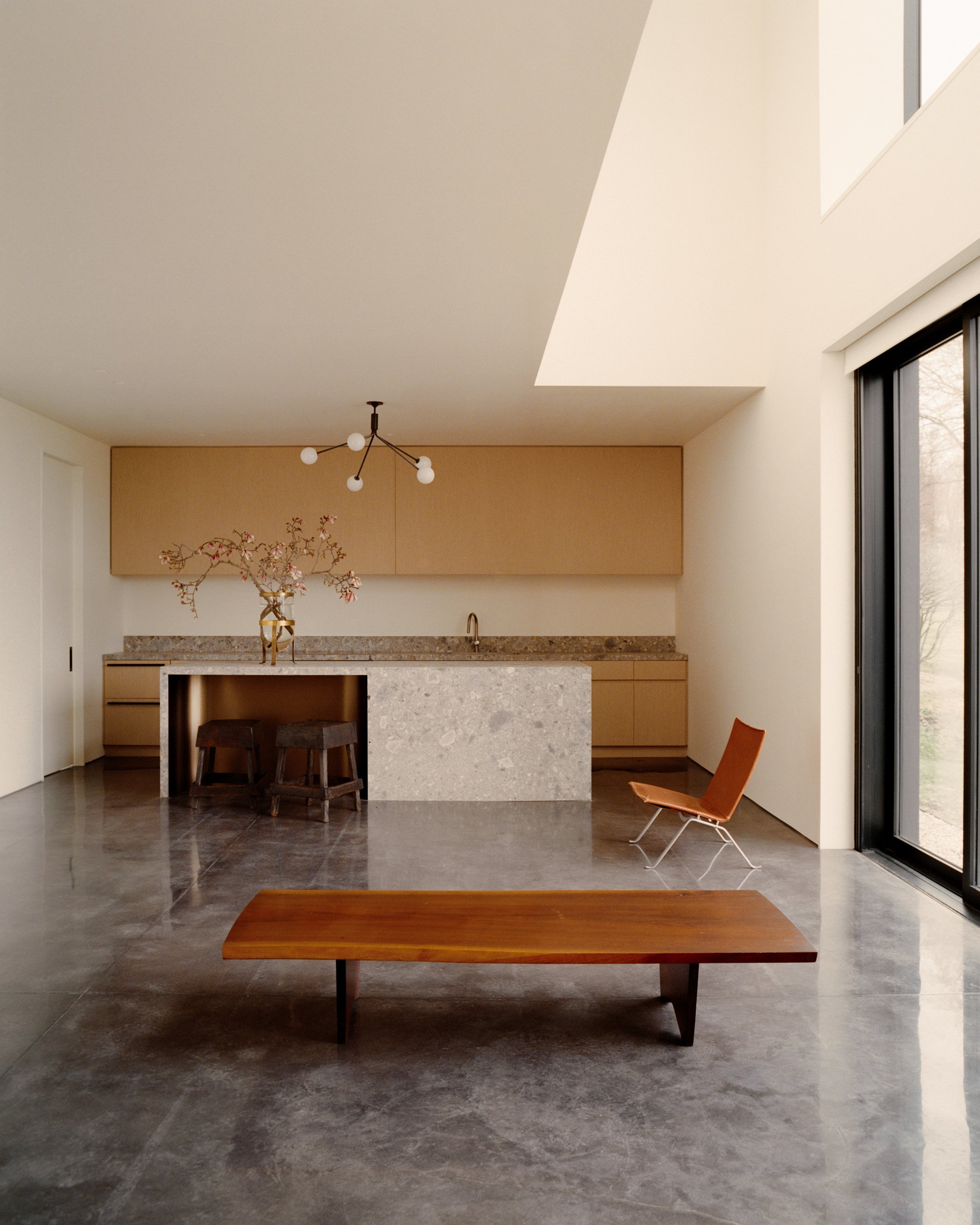 Kitchen with a stone waterfall island and warm-toned cabinetry on polished concrete floors at a Ghent, NY home by JG Neukomm Architecture
