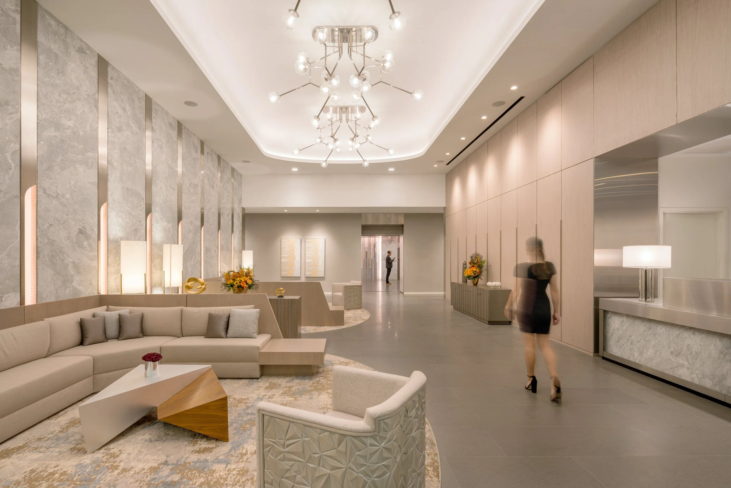 GNA residential lobby lounge with a curved sectional, faceted accent chair, sputnik chandelier, and marble walls